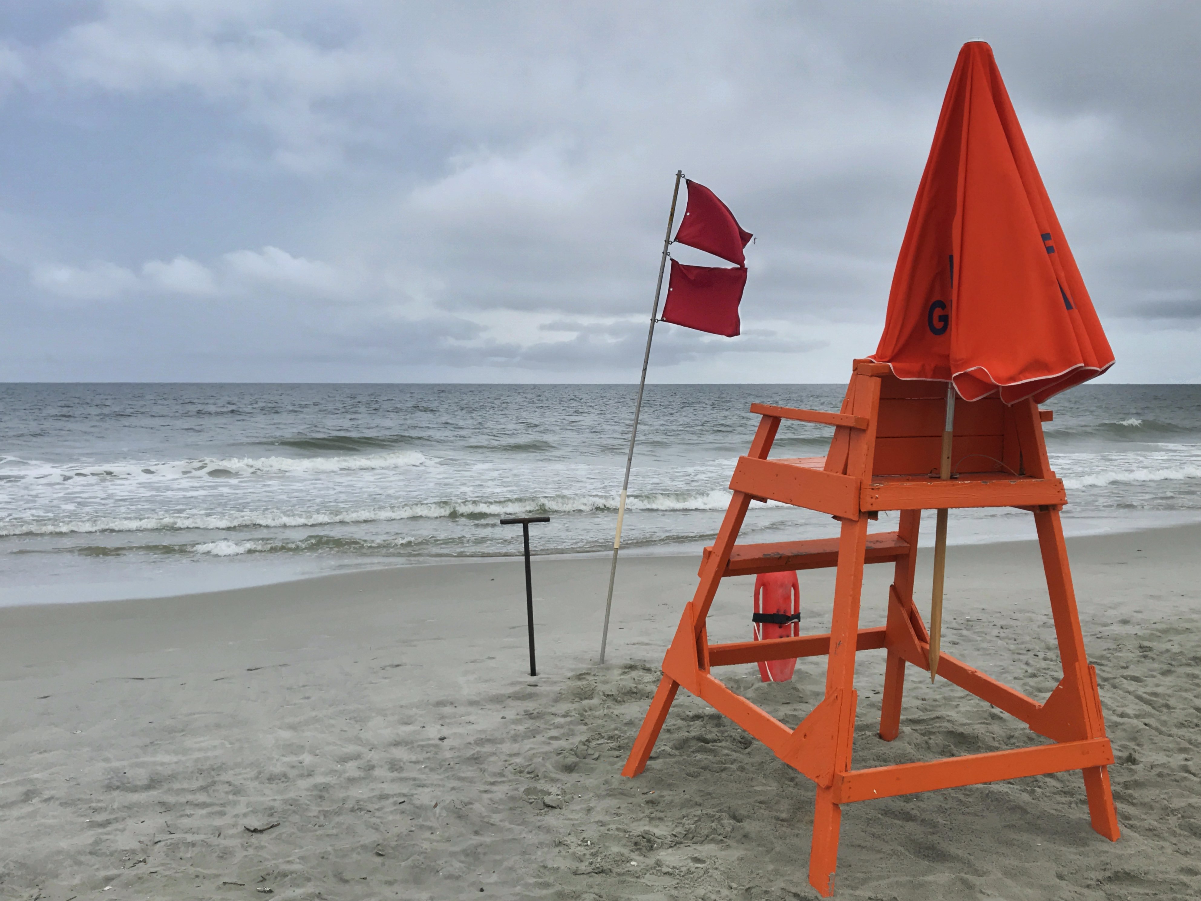 Playa con silla de salvavidas, sombrilla, y banderillas rojas señalando un mar peligroso. | Foto: Shutterstock