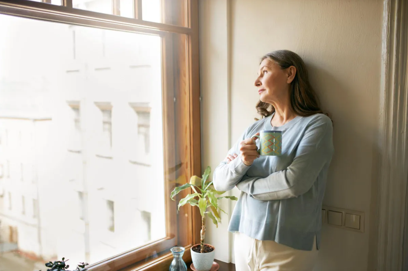 Mujer madura de pie cerca de una ventana | Fuente: Freepik