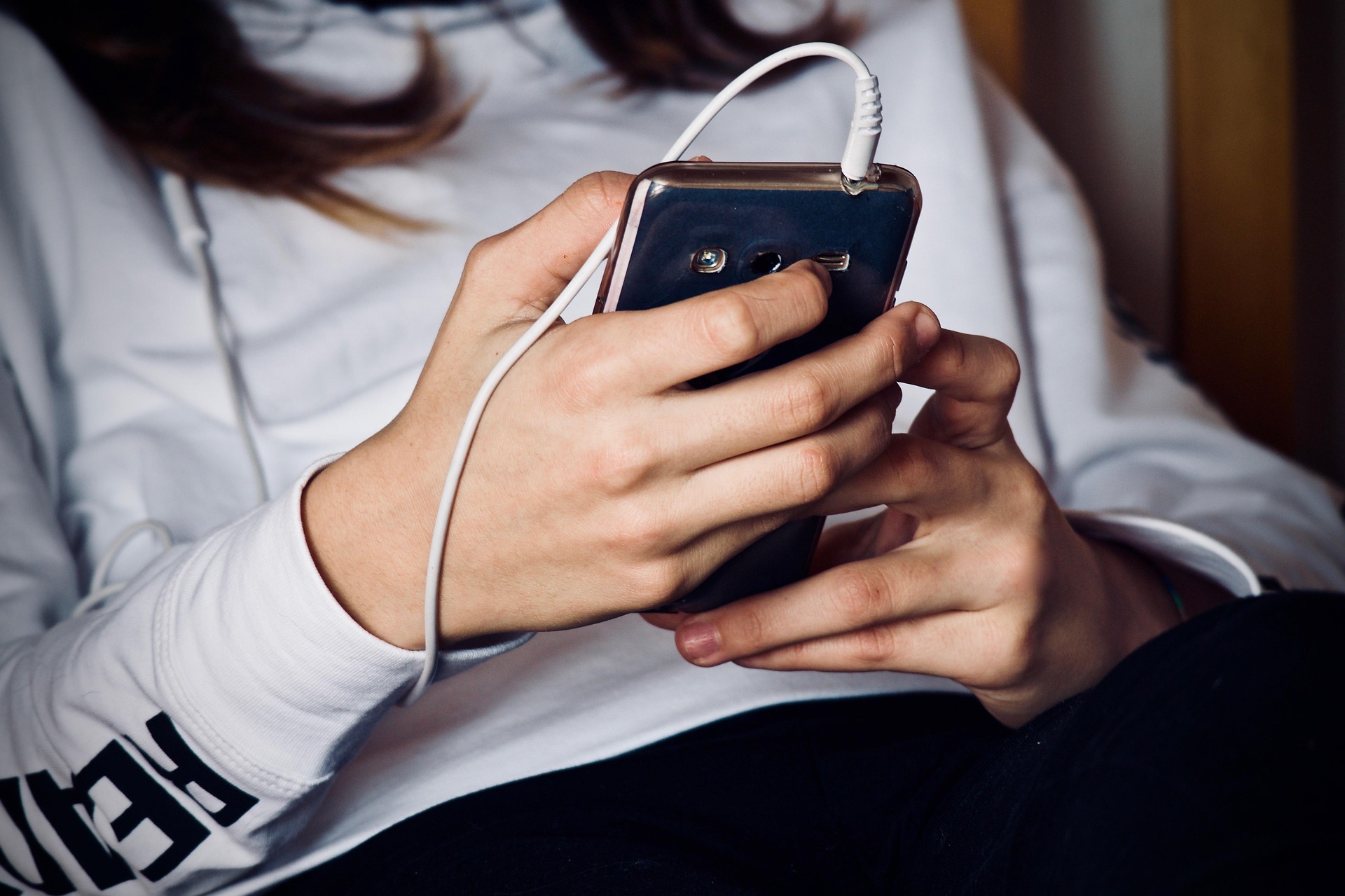 Una mujer mirando un teléfono con auriculares conectados | Foto: Pixabay