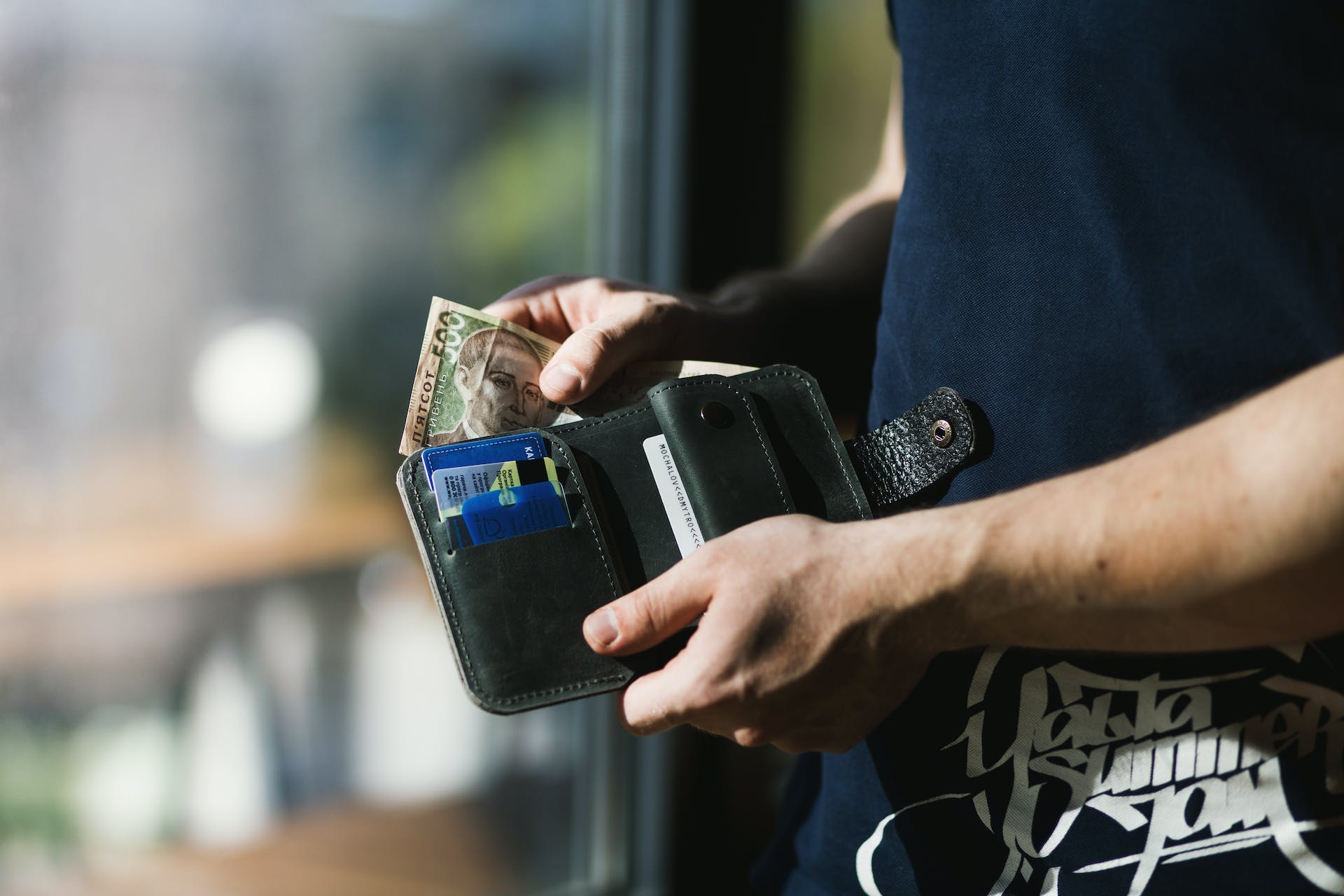 Persona sosteniendo una cartera de cuero negro con dinero | Foto: Pexels
