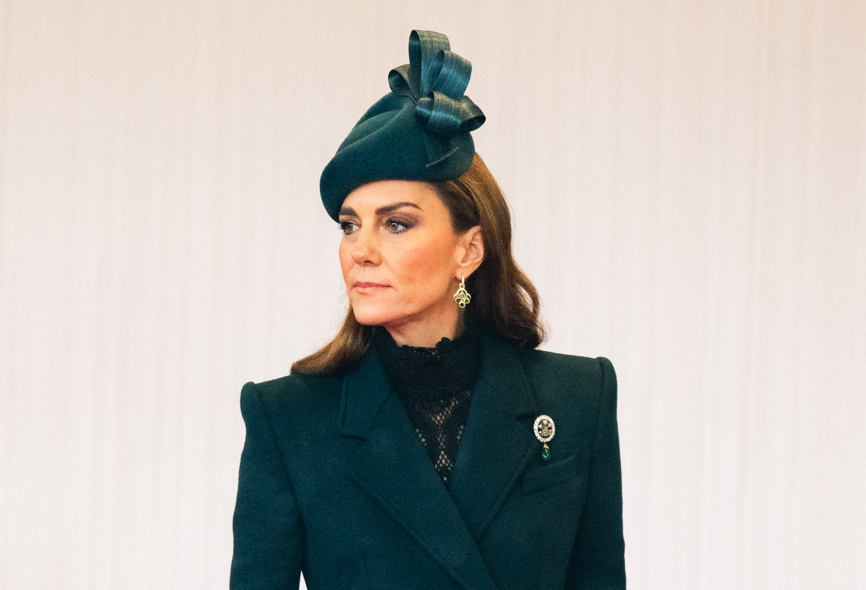 Un primer plano muestra a Catherine, princesa de Gales, el 20 de octubre de 2026, en el que destaca el elaborado estilo de su look de día. Su abrigo a medida con solapas en V enmarca un cuello alto de encaje negro transparente, acompañado de un tocado escultural con un lazo verde, unos pendientes tipo candelabro de Cassandra Goad y el brillante broche "Prince of Wales Feathers" sujeto a su hombro izquierdo. | Fuente: Getty Images