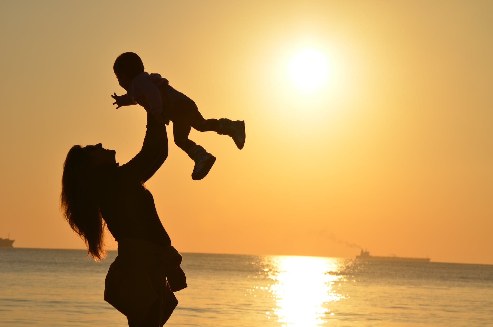 Silueta de una madre llevando a su bebé en la playa durante la hora dorada | Foto: Pexels
