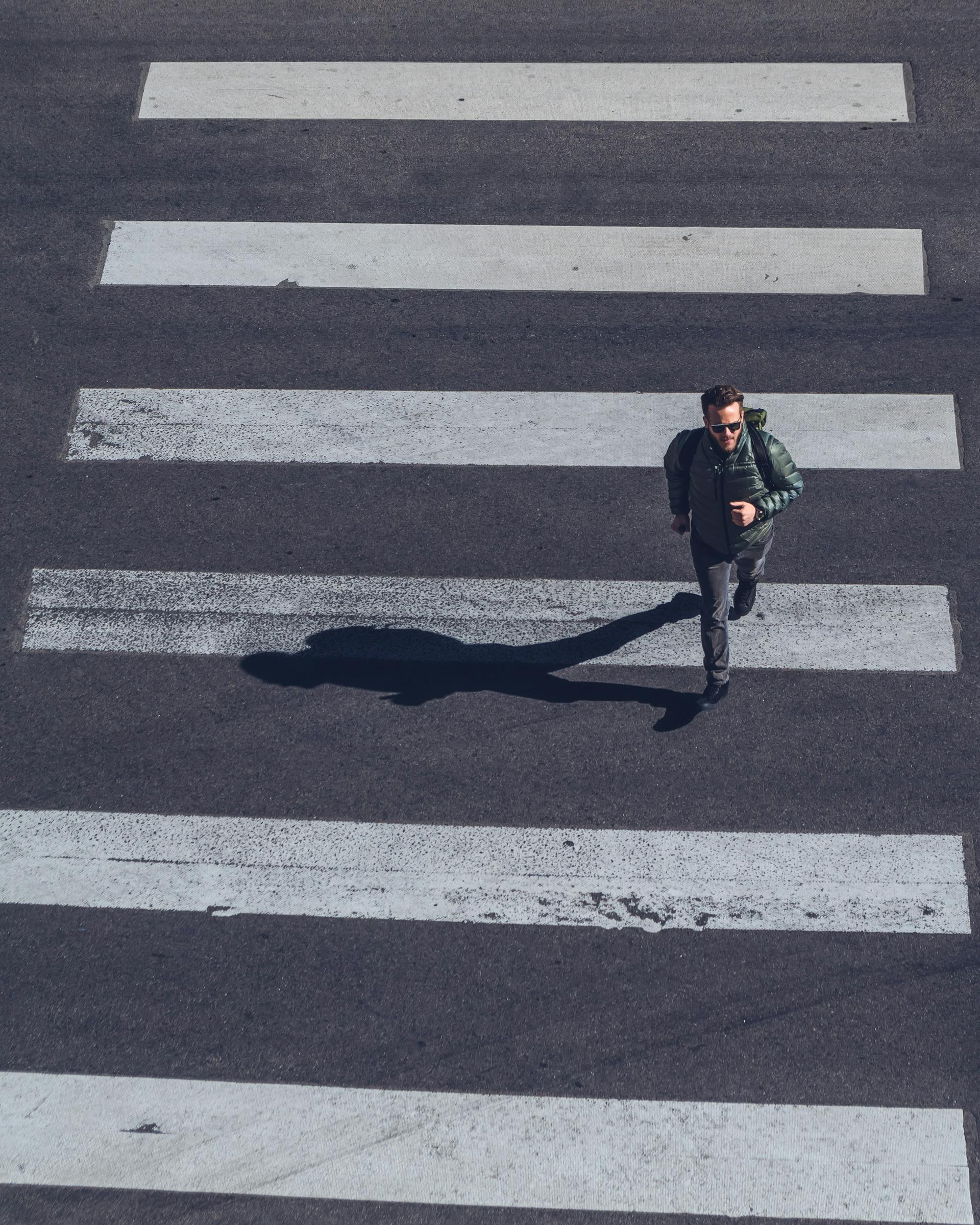 Un hombre apresurándose sobre un paso de peatones | Fuente: Pexels