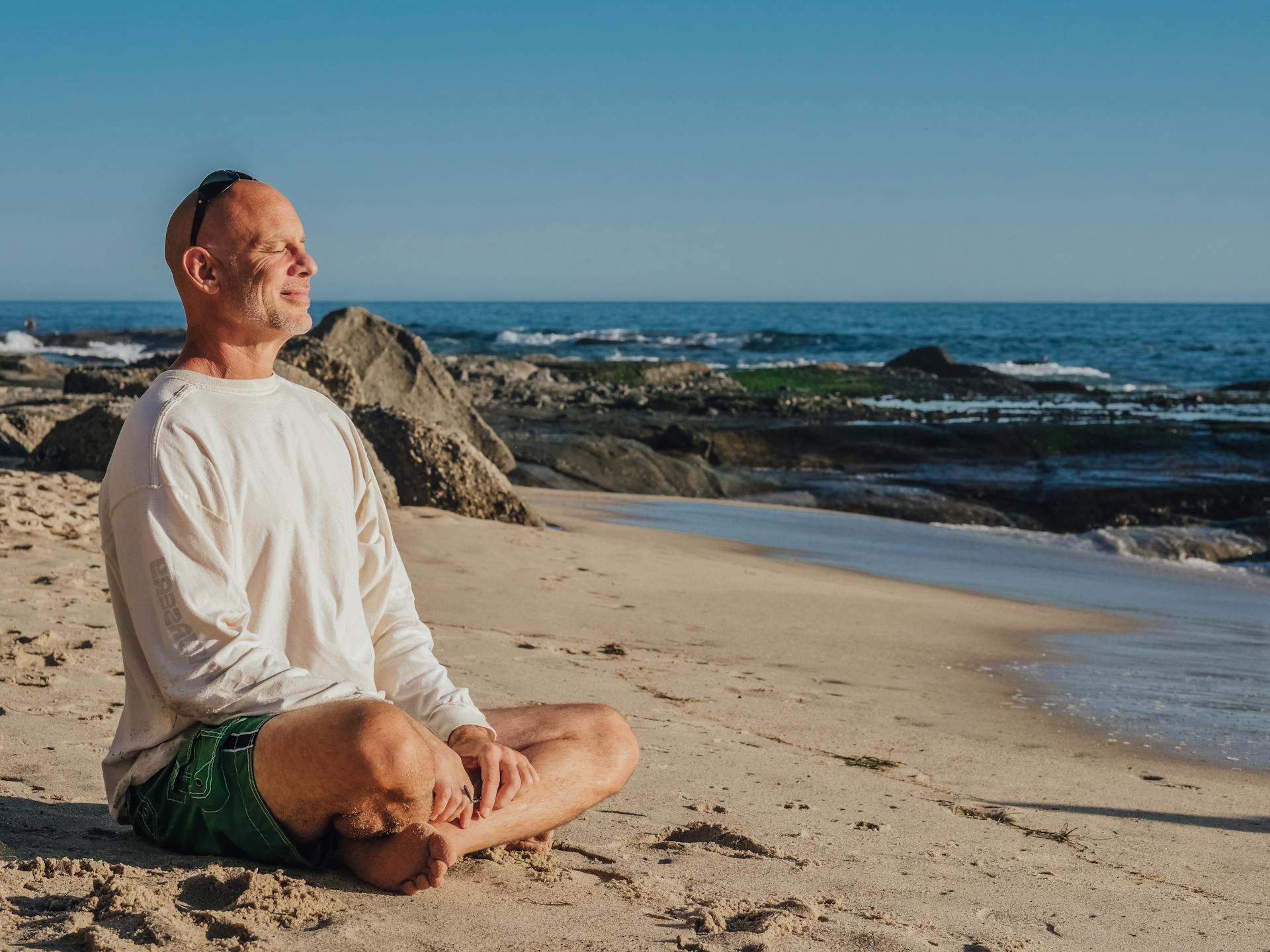 Un hombre sonríe mientras hace yoga en la playa | Fuente: Pexels