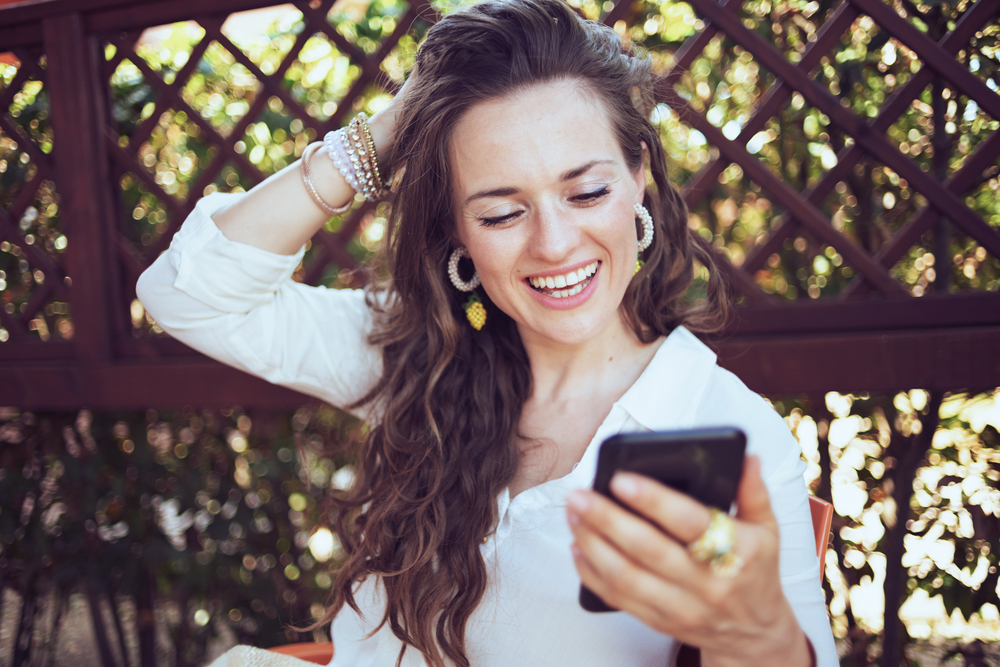 Mujer sonriendo mientras usa su teléfono | Fuente: Shutterstock