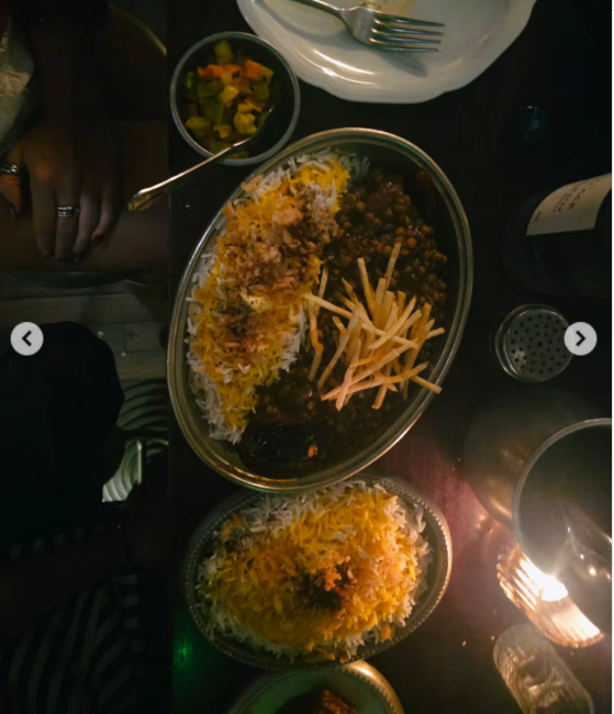 Una toma cenital capturó una apetitosa propuesta gastronómica servida en fuentes metálicas ovaladas sobre una mesa iluminada a la luz de las velas. El plato principal incluye una combinación de arroz basmati especiado acompañado por guiso de legumbres y carne, decorado en el centro con finas papas pay crujientes. | Fuente: Instagram/emilia_att