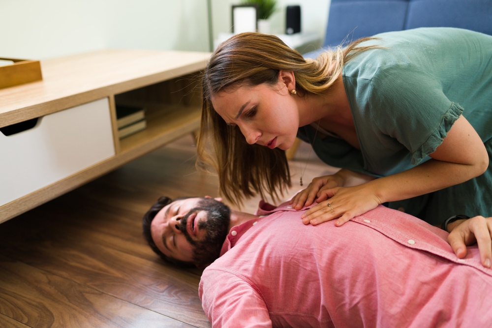 ¿Estás respirando? Mujer joven y atractiva revisando a un hombre inconsciente en el suelo. | Fuente: Shutterstock