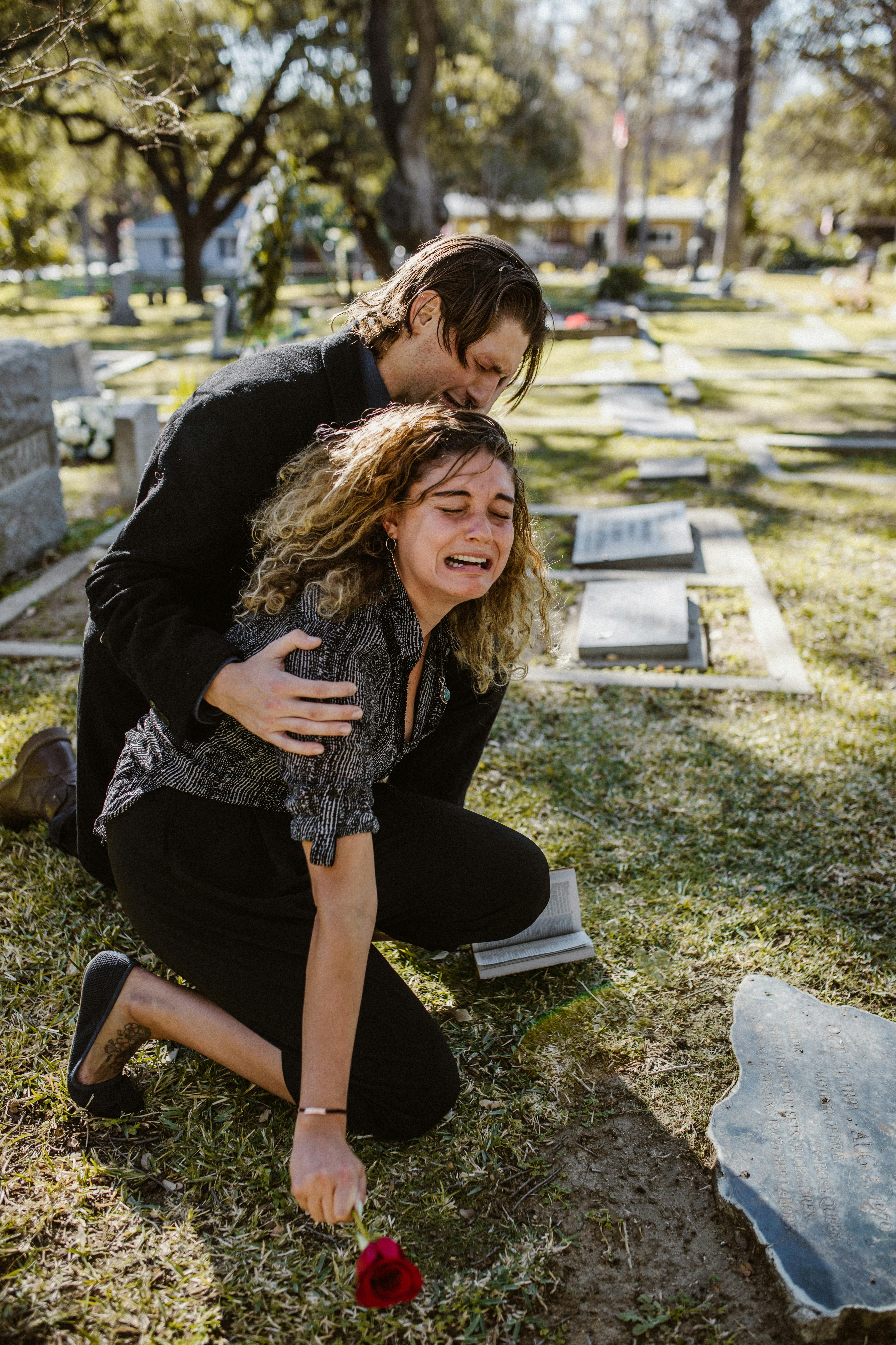 Una joven consolada por un hombre mientras llora en una tumba | Foto: Pexels