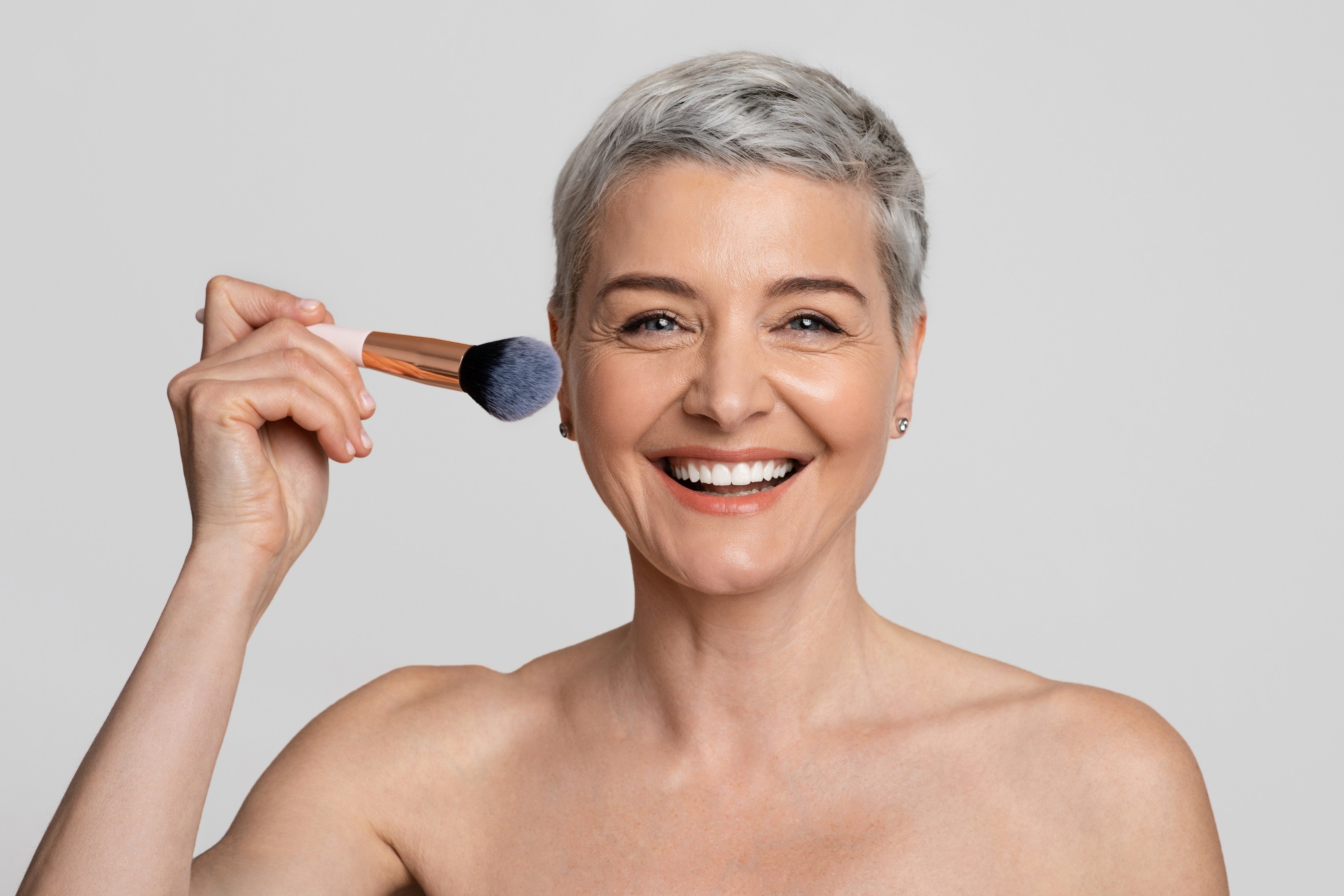 Mujer con cabello gris se aplica rubor. | Foto: Shutterstock