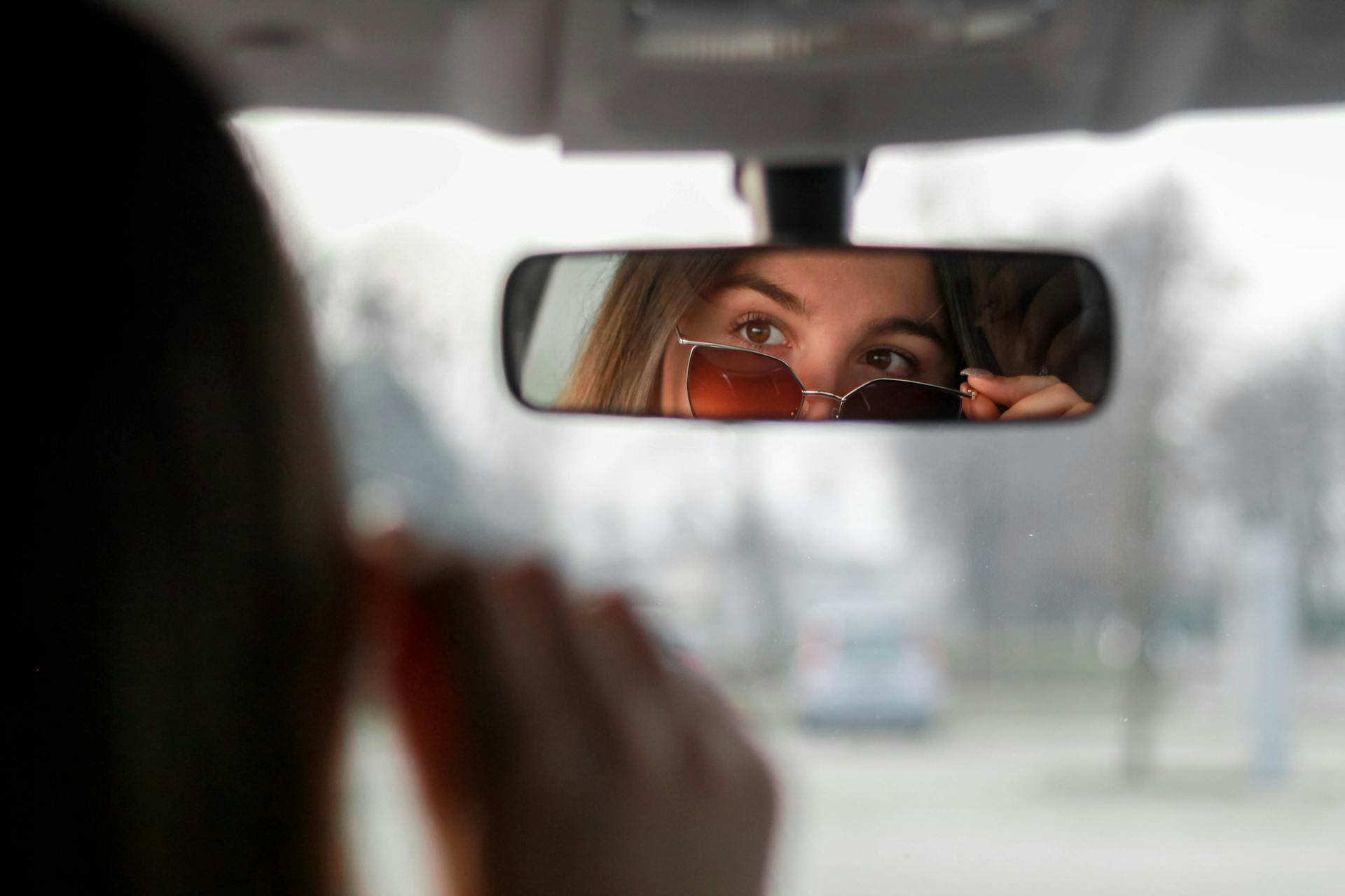 Mujer segura de sí misma con gafas de sol mirando su reflejo en el espejo retrovisor | Fuente: Pexels