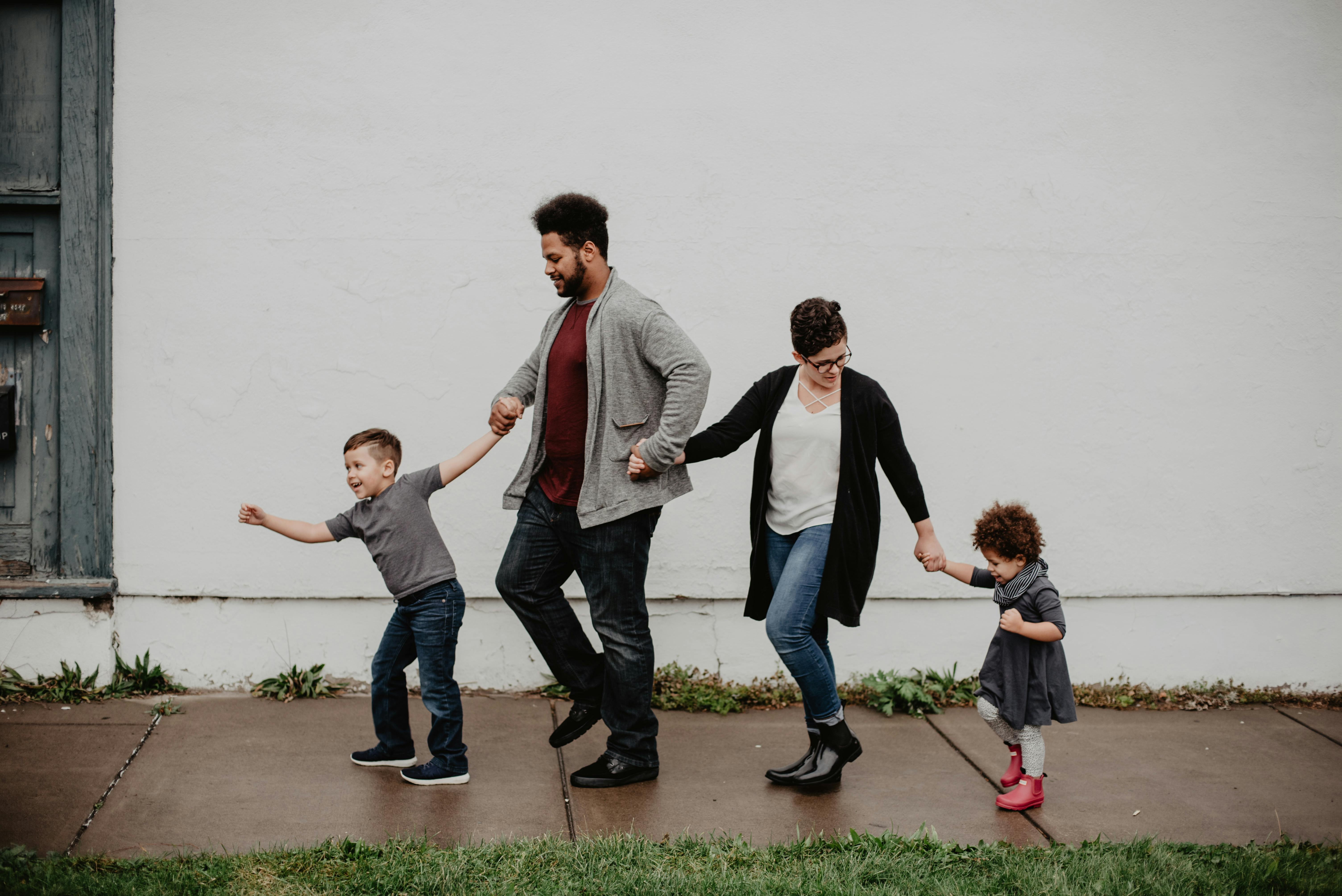 Una familia de cuatro cogidos de la mano y caminando | Fuente: Pexels