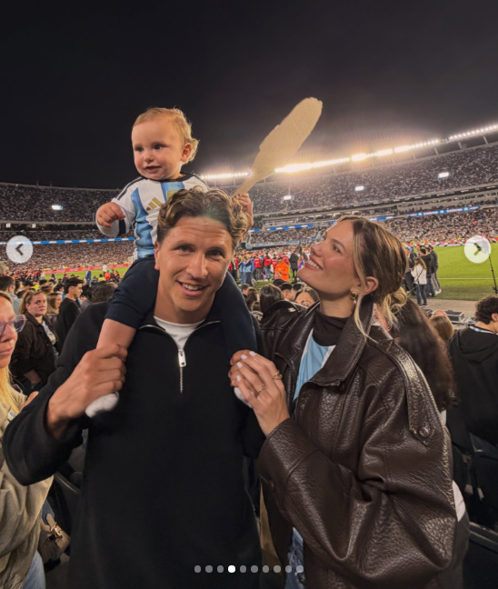 Eva Bargiela miró con complicidad y una tierna sonrisa a su esposo mientras él sostenía a su hijo Faustino sobre sus hombros en plena tribuna. La modelo lució una campera oversize de cuero marrón, mientras el pequeño sonreía hacia la cámara agitando una pancarta en medio de la hinchada. | Fuente: Instagram/evabargiela