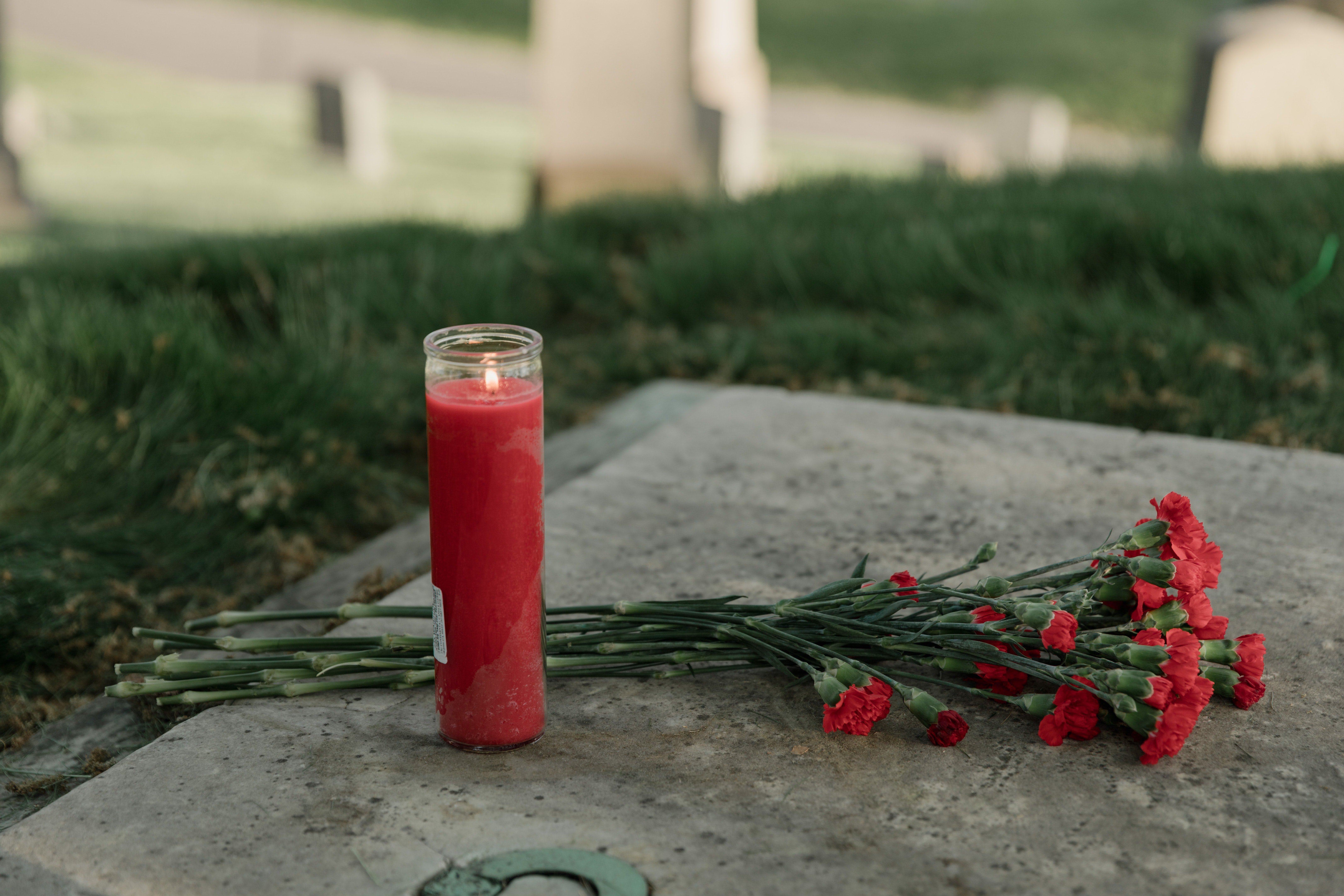 Un velón rojo y unas flores sobre una lápida. | Foto: Pexels