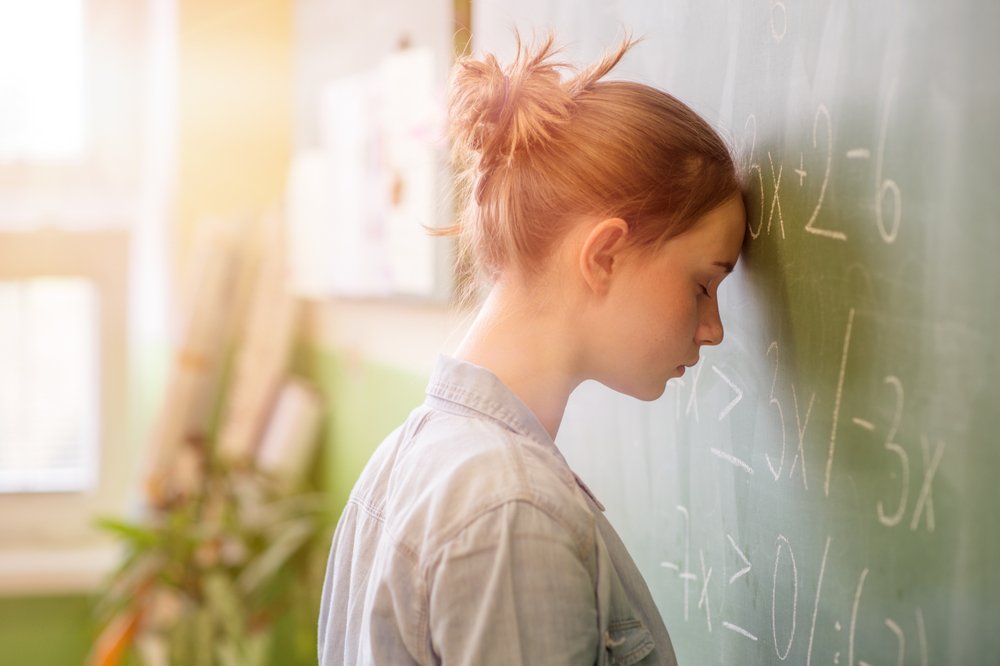 Chica adolescente en la clase de matemáticas abrumada por fórmula matemática. Fuente: Shutterstock