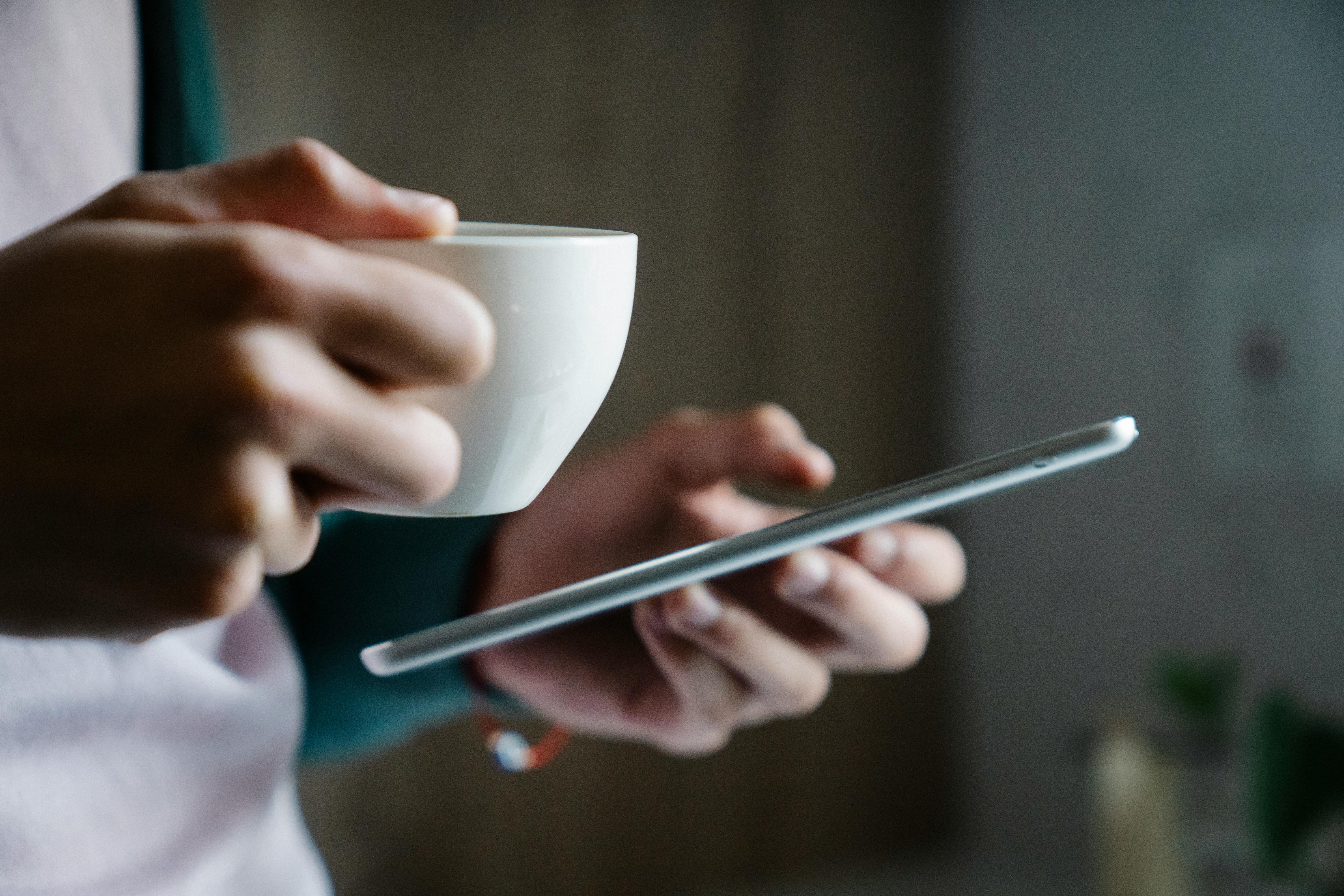 Primer plano de una persona con una taza de café en la mano y un smartphone | Fuente: Pexels