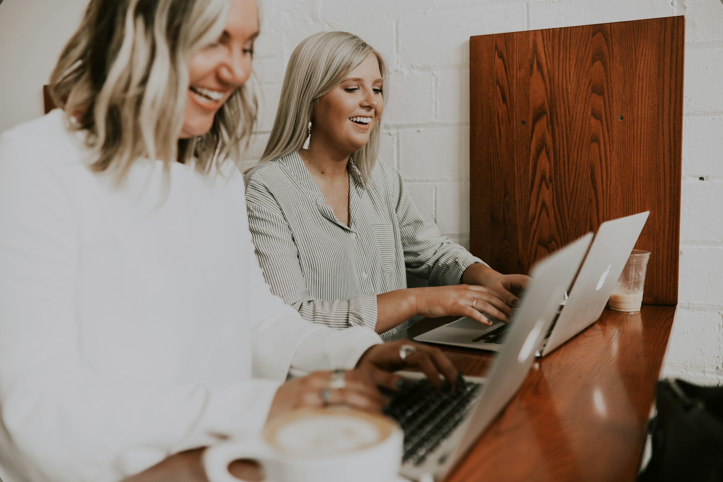 Dos mujeres ríen mientras usan sus portátiles en una oficina | Fuente: Unsplash