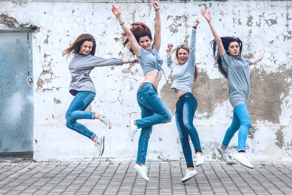 Cuatro mujeres saltando vestidas con pantalones de jean, camisetas y zapatos deportivos. | Foto: Shutterstock