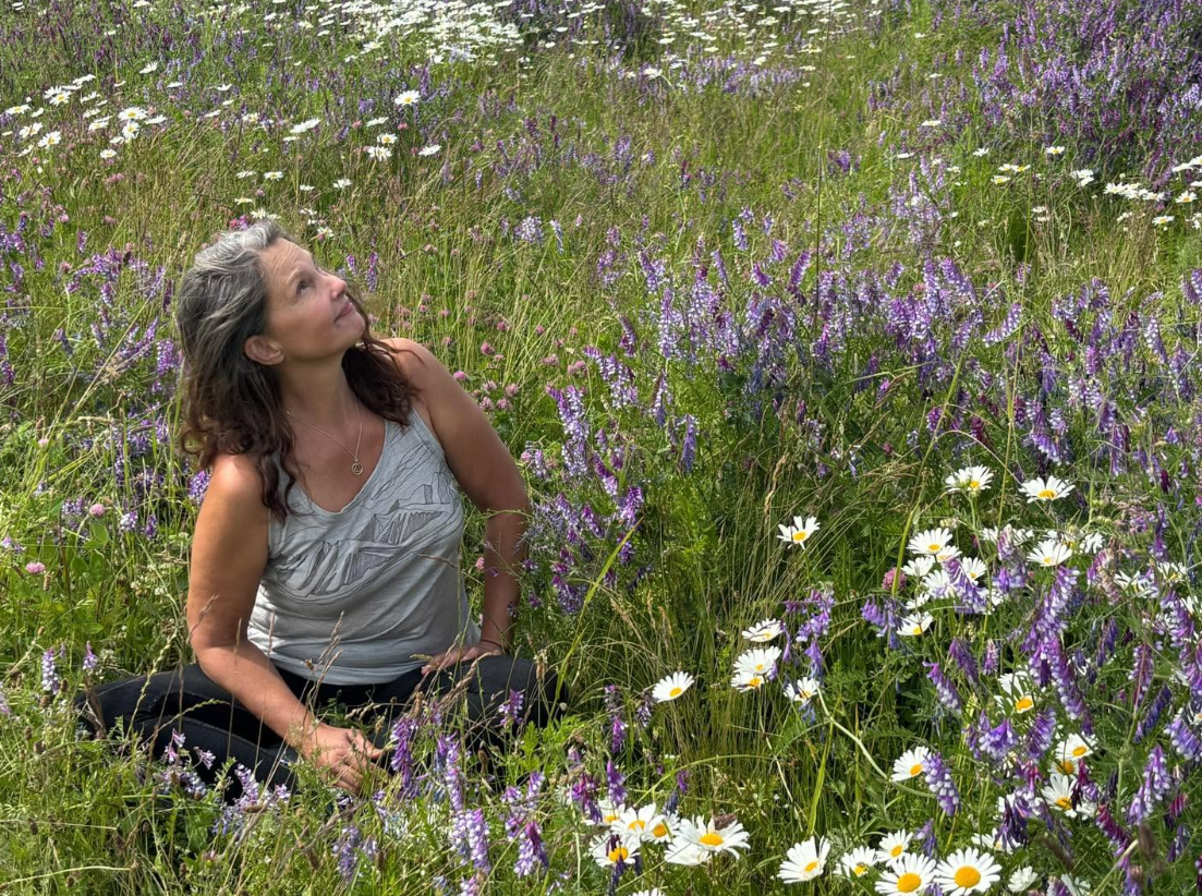 En 2026, sentada entre flores silvestres moradas y margaritas blancas, Judd mira hacia el cielo con su pelo con mechas grises cayéndole suelto sobre los hombros. Este escenario al aire libre permite echar un vistazo a su vida lejos de los eventos de Hollywood. | Fuente: Facebook/AshleyJuddOfficial