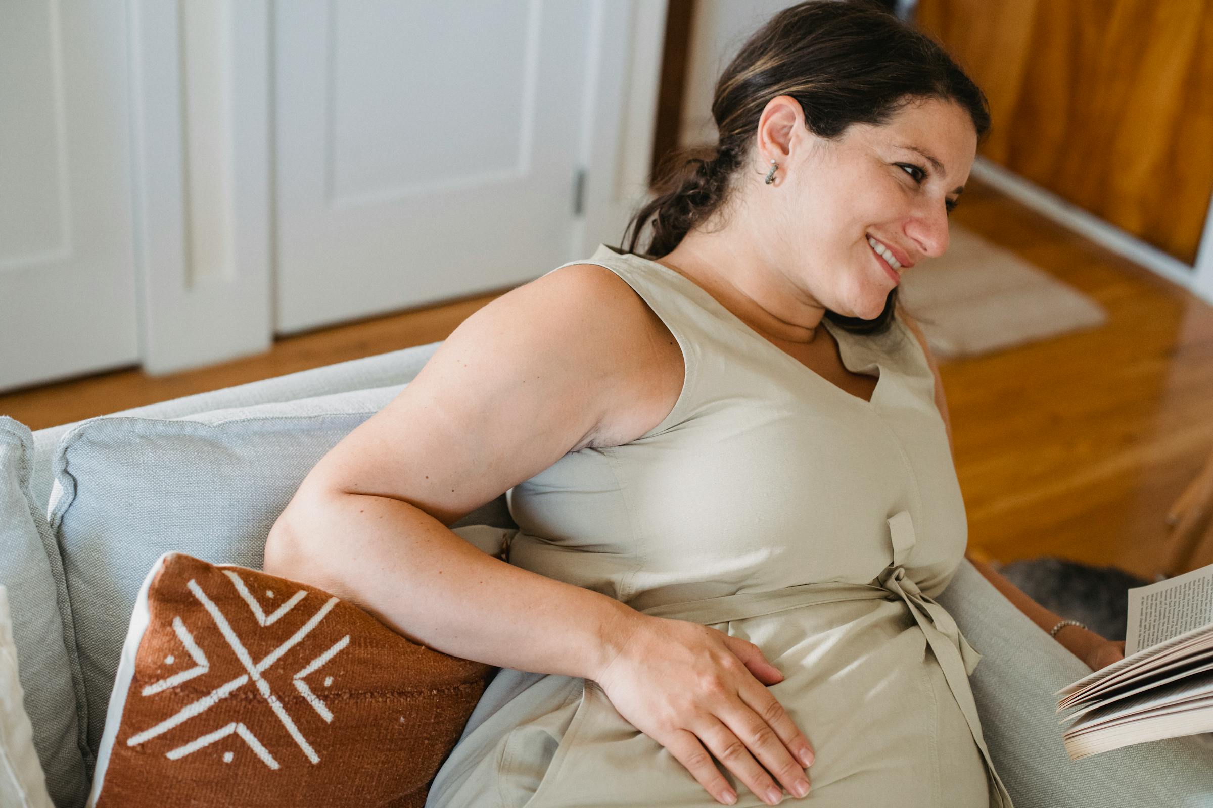 Una mujer embarazada sonriendo y sentada en un sofá | Fuente: Pexels