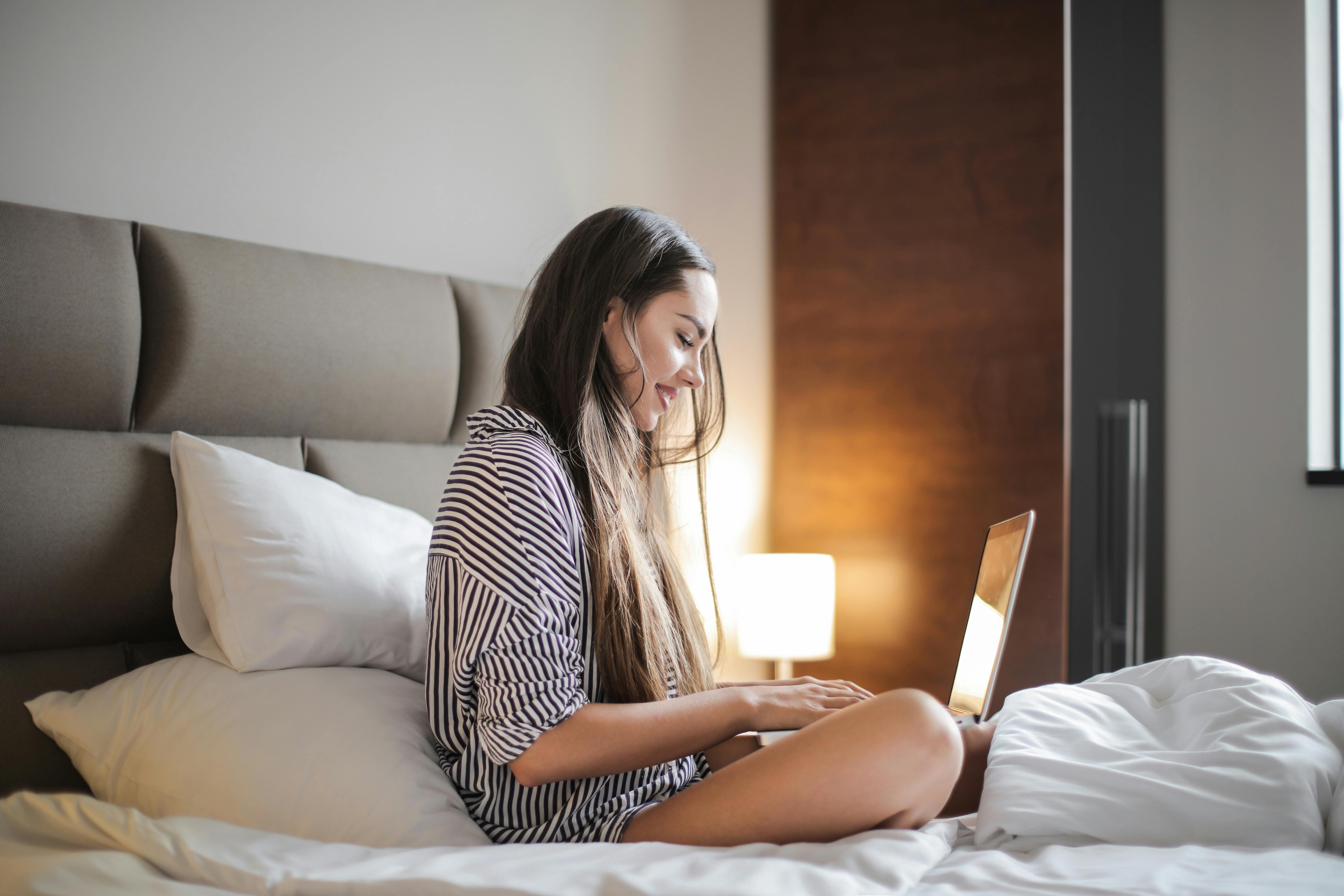 Una mujer sentada en la cama y utilizando su ordenador portátil | Fuente: Pexels