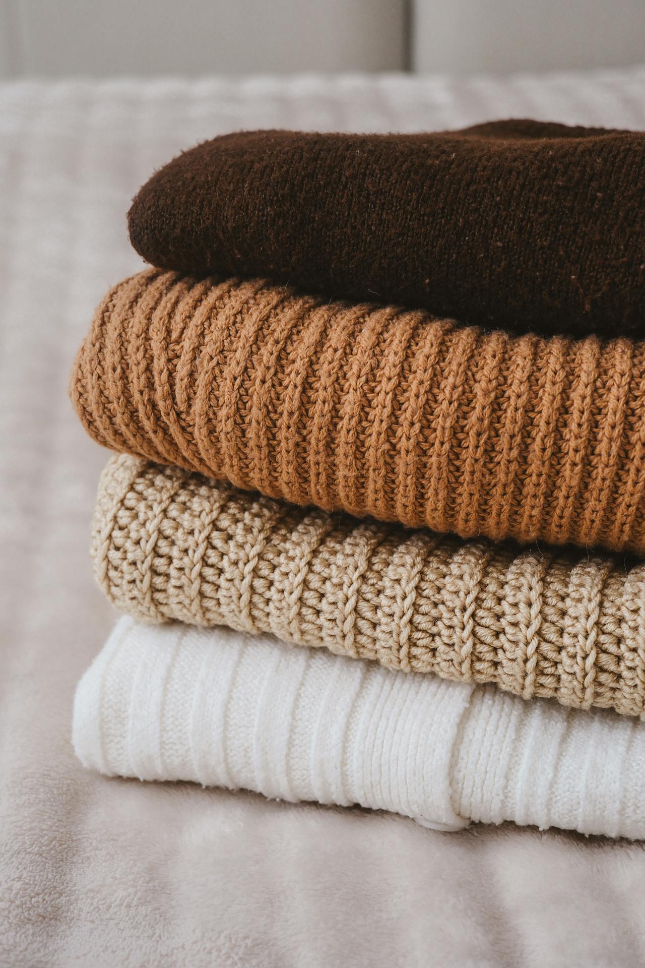 Una pila de jerséis doblados sobre la cama | Fuente: Pexels