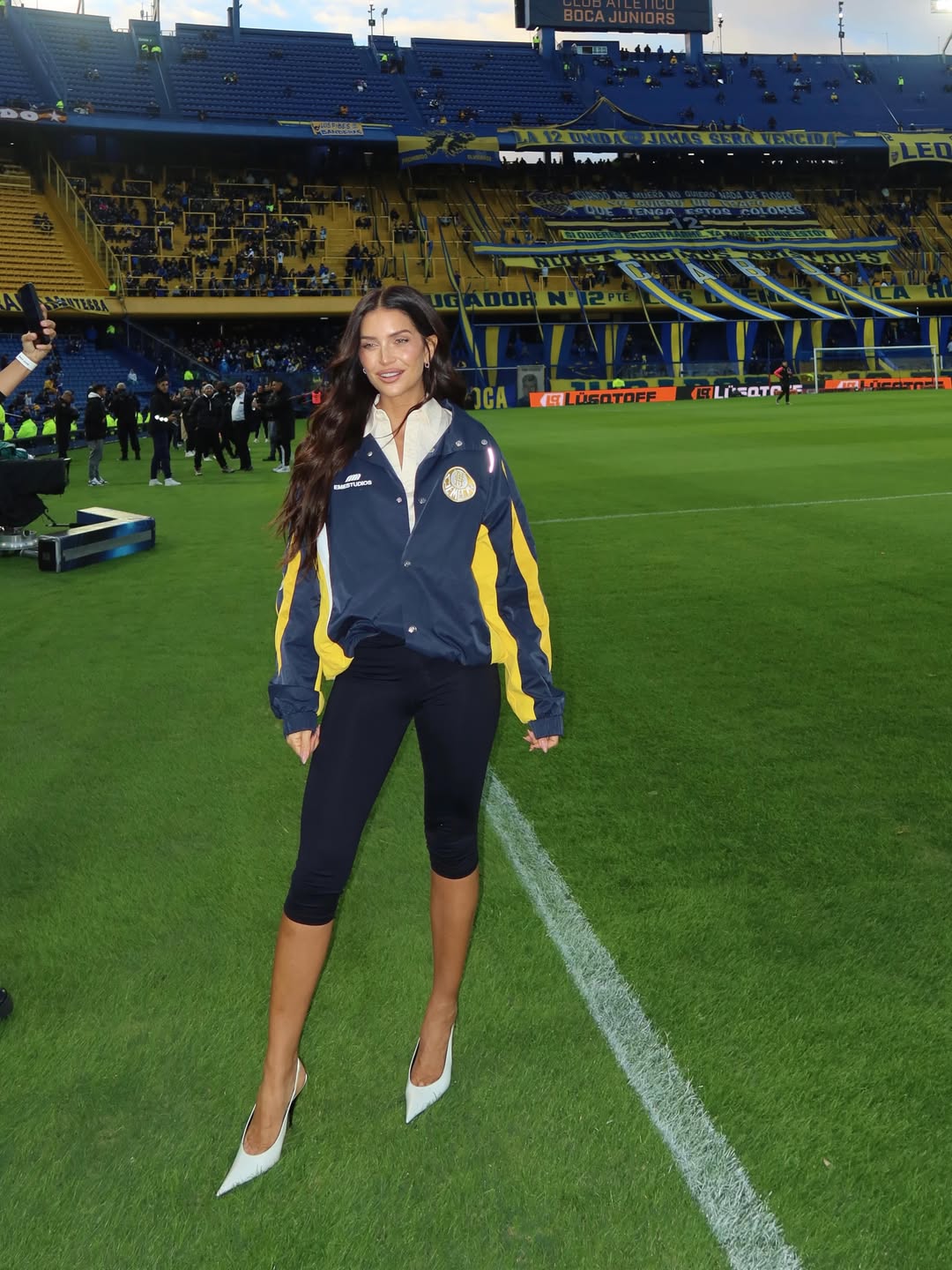 Zaira Nara posa en el campo de juego de La Bombonera durante su visita al estadio de Boca Juniors con un look deportivo combinado con stilettos blancos. | Fuente: Instagram/zaira.nara