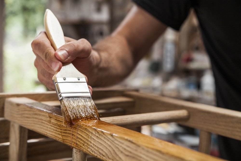 Hombre sosteniendo un pincel oara aplicar pintura de barniz en muebles de madera. | Fuente: shutterstock