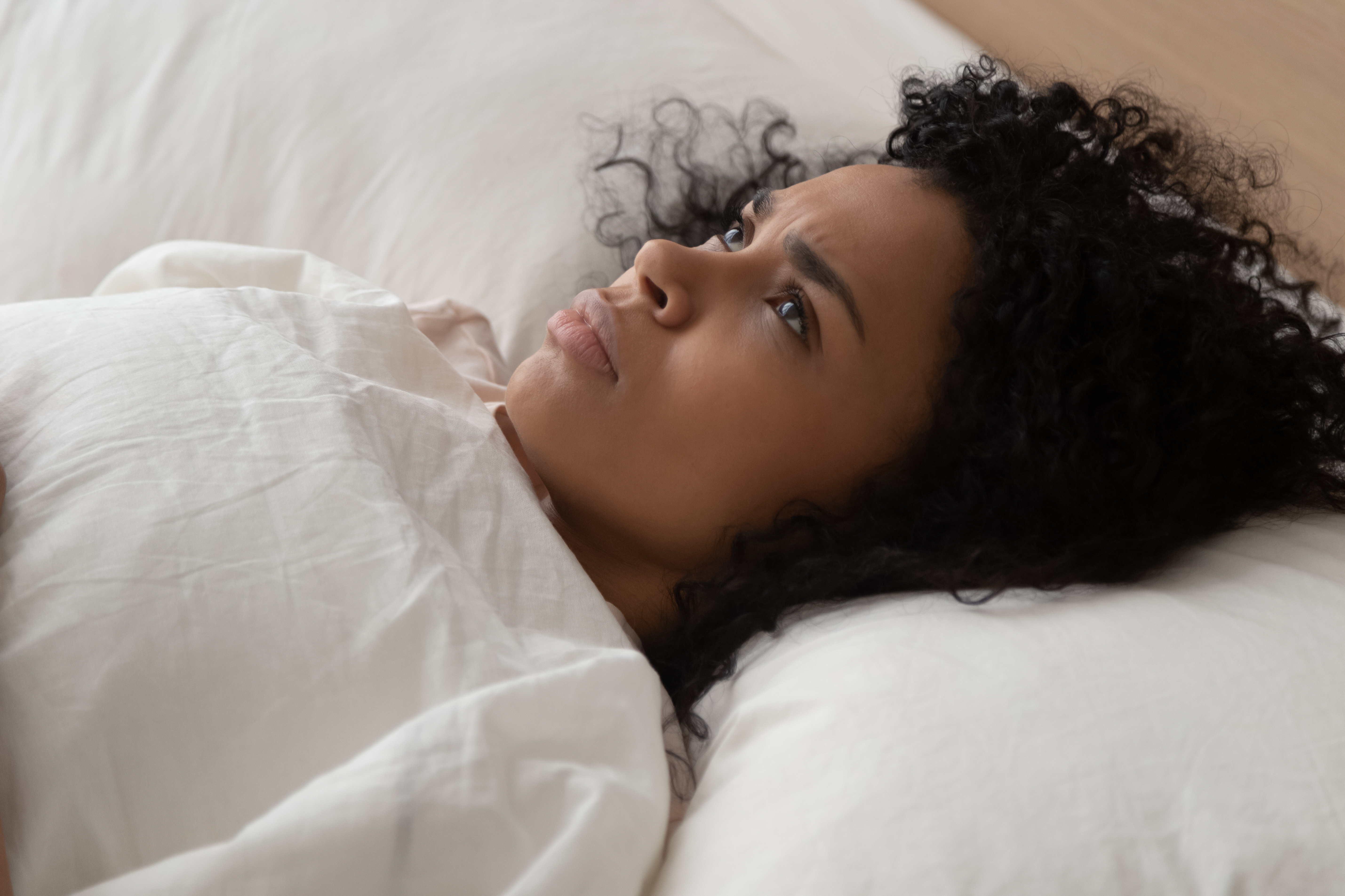 Una mujer negra mirando hacia arriba mientras tiene problemas para conciliar el sueño | Fuente: Shutterstock