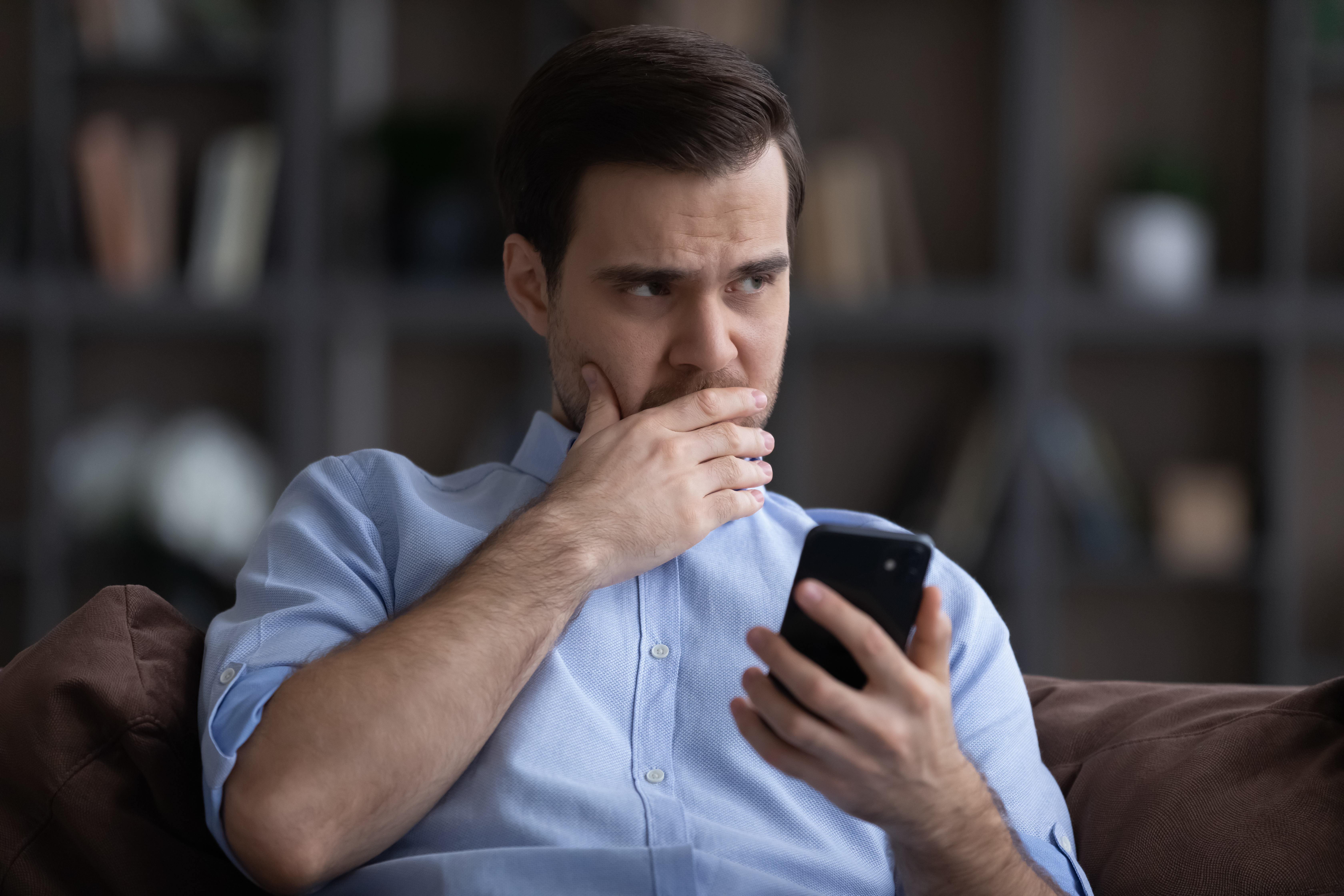 Un hombre ansioso pensando mientras sostiene su teléfono | Fuente: Shutterstock