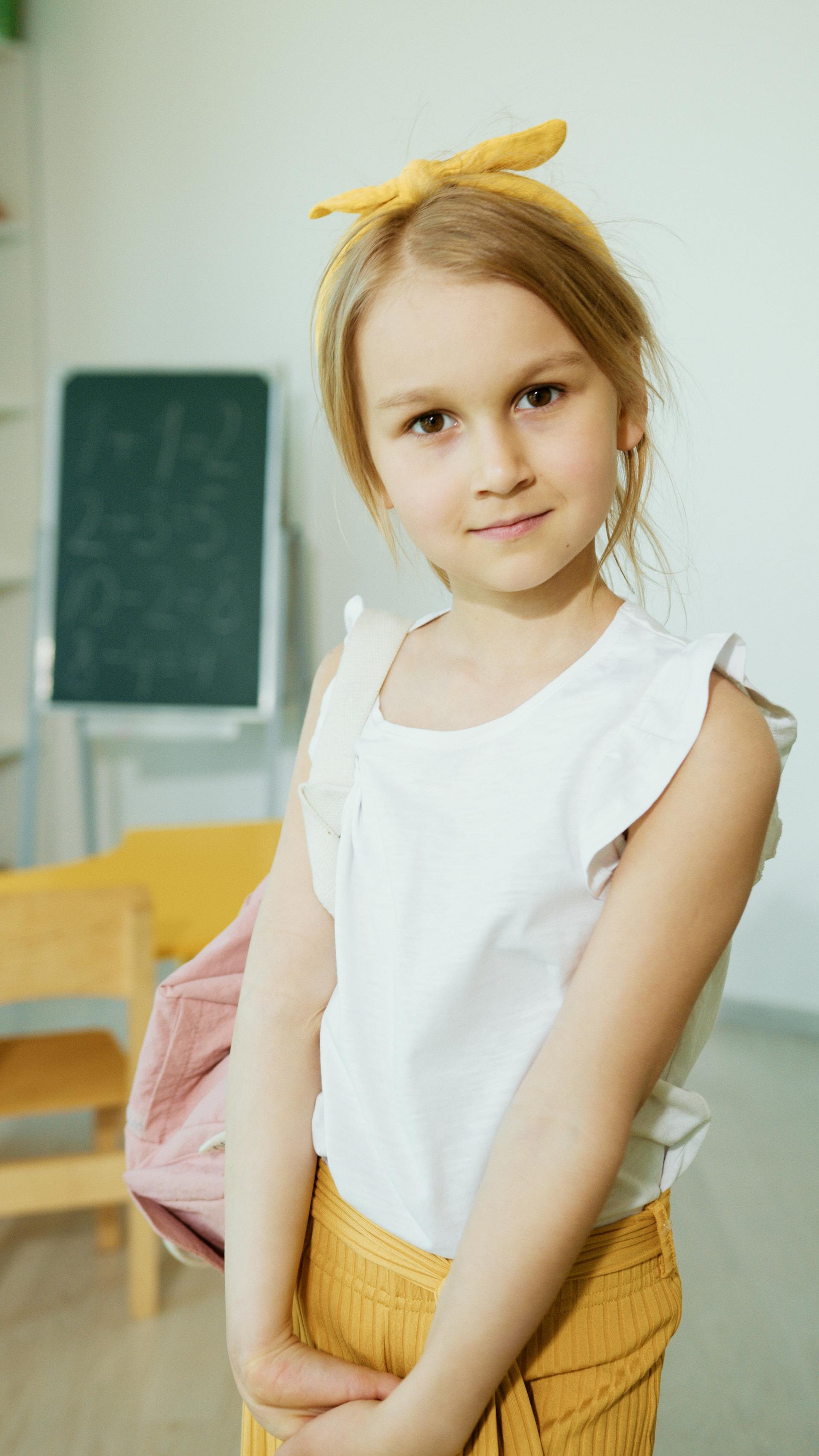 Una niña con una blusa blanca sin mangas sonriendo en una habitación | Fuente: Pexels