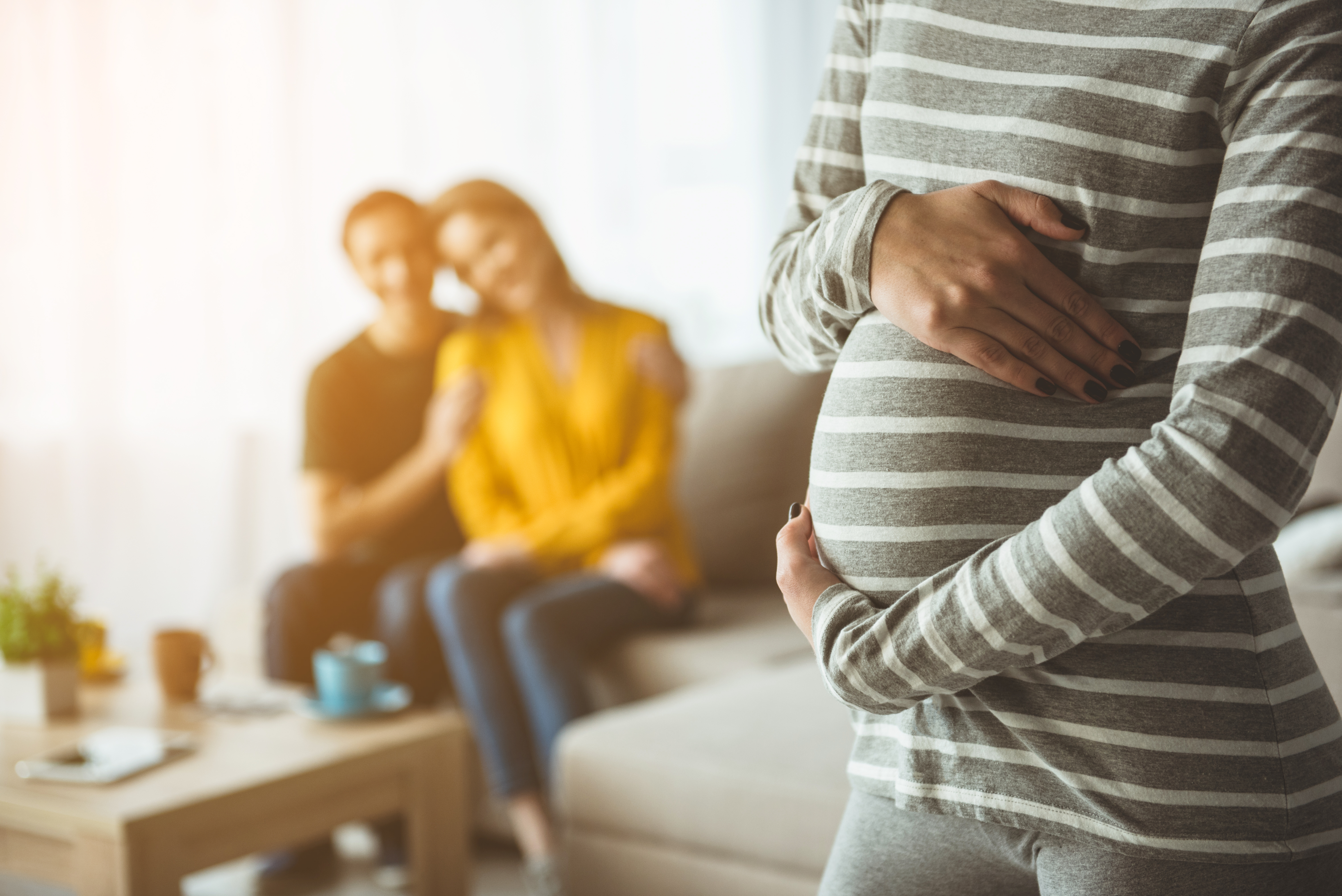 Una mujer embarazada rodea su barriguita con una feliz pareja al fondo. | Foto: Shutterstock