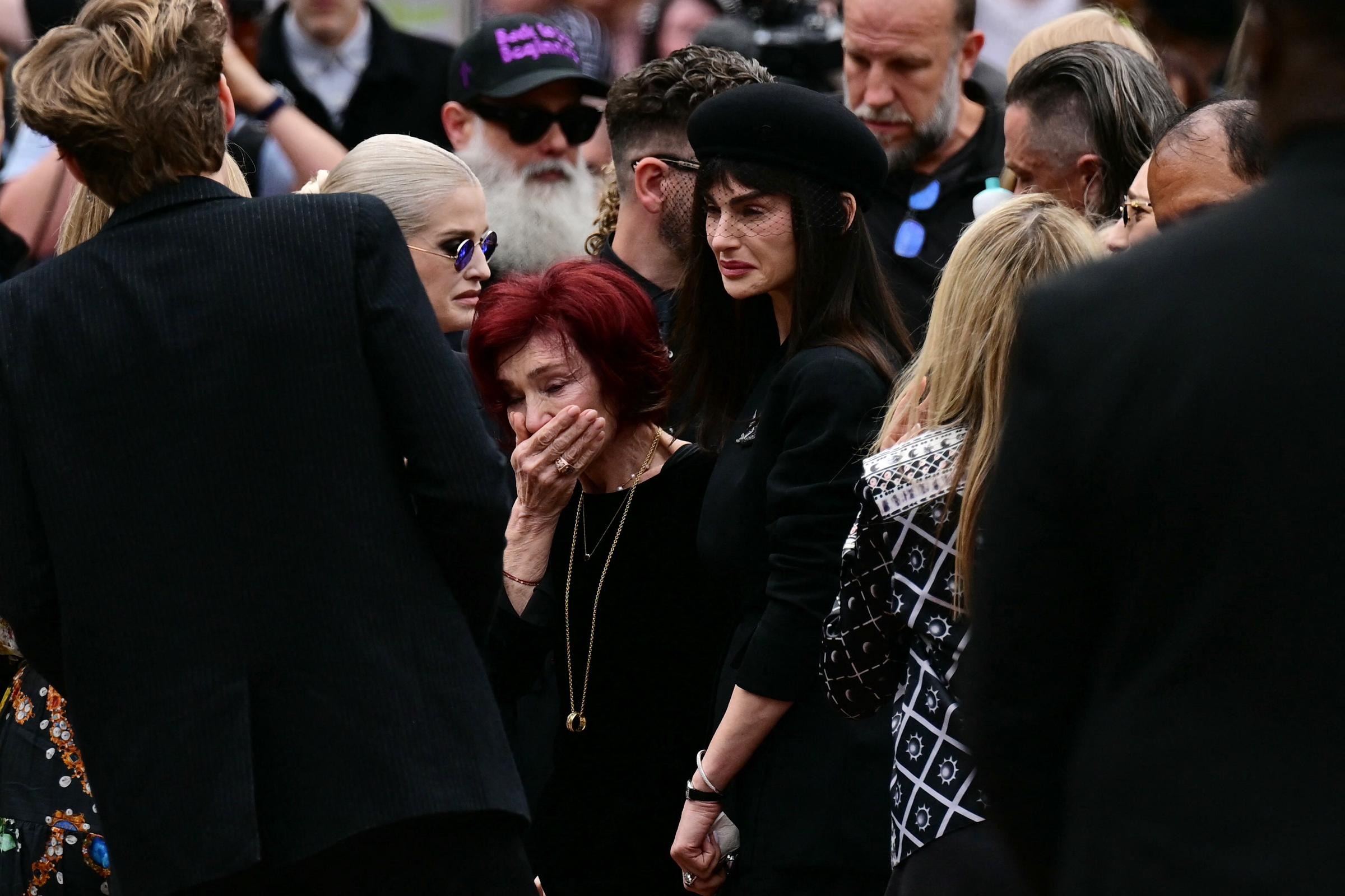 Sharon, Kelly y Aimee Osbourne reaccionan ante los homenajes dejados en el banco del puente de Black Sabbath durante el cortejo fúnebre de Ozzy en Birmingham el 30 de julio de 2025 | Fuente: Getty Images
