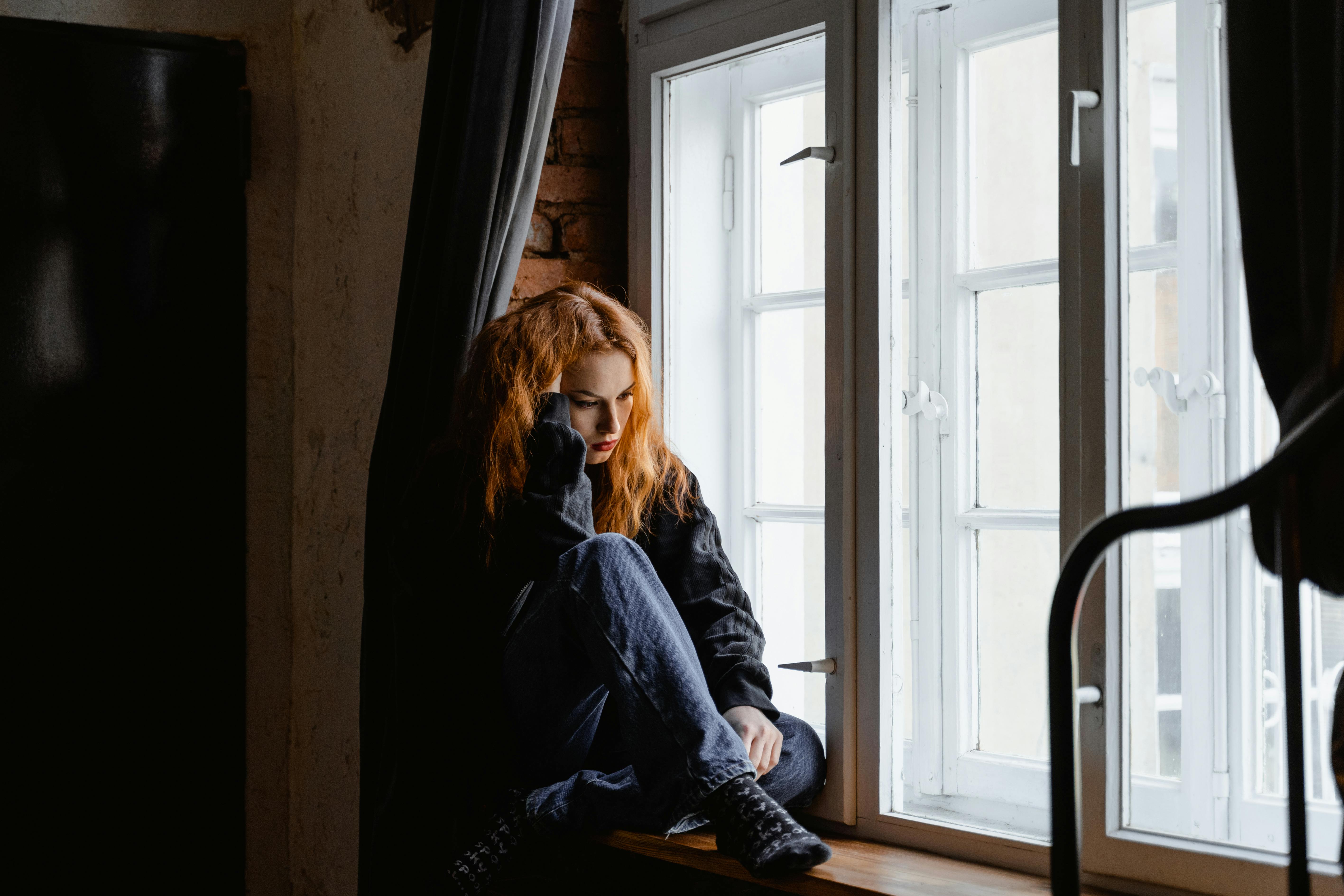 Una mujer con cara de disgusto sentada junto a una ventana | Fuente: Pexels