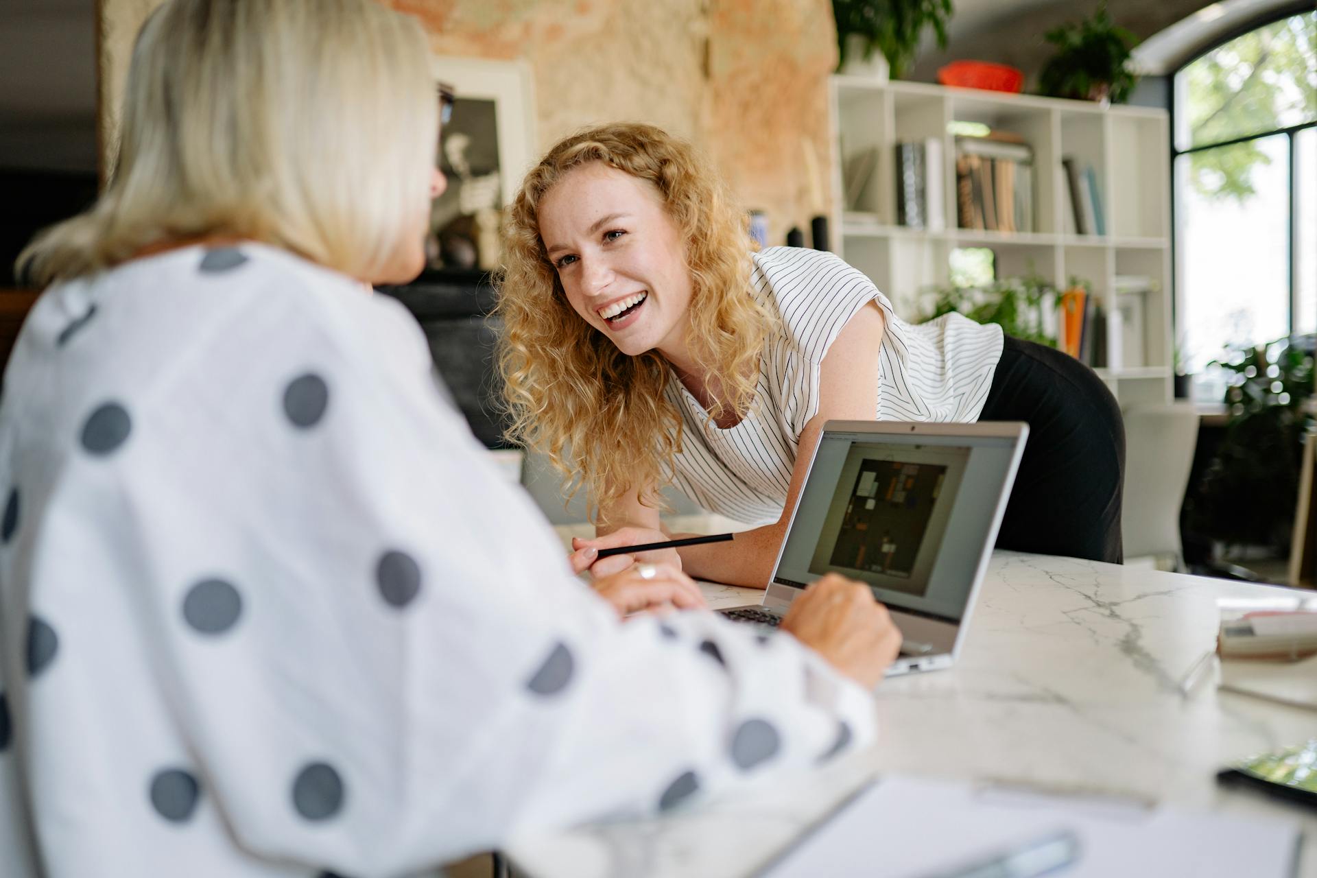 Una mujer riendo apoyada en una mesa mientras habla con su compañero de trabajo | Fuente: Pexels
