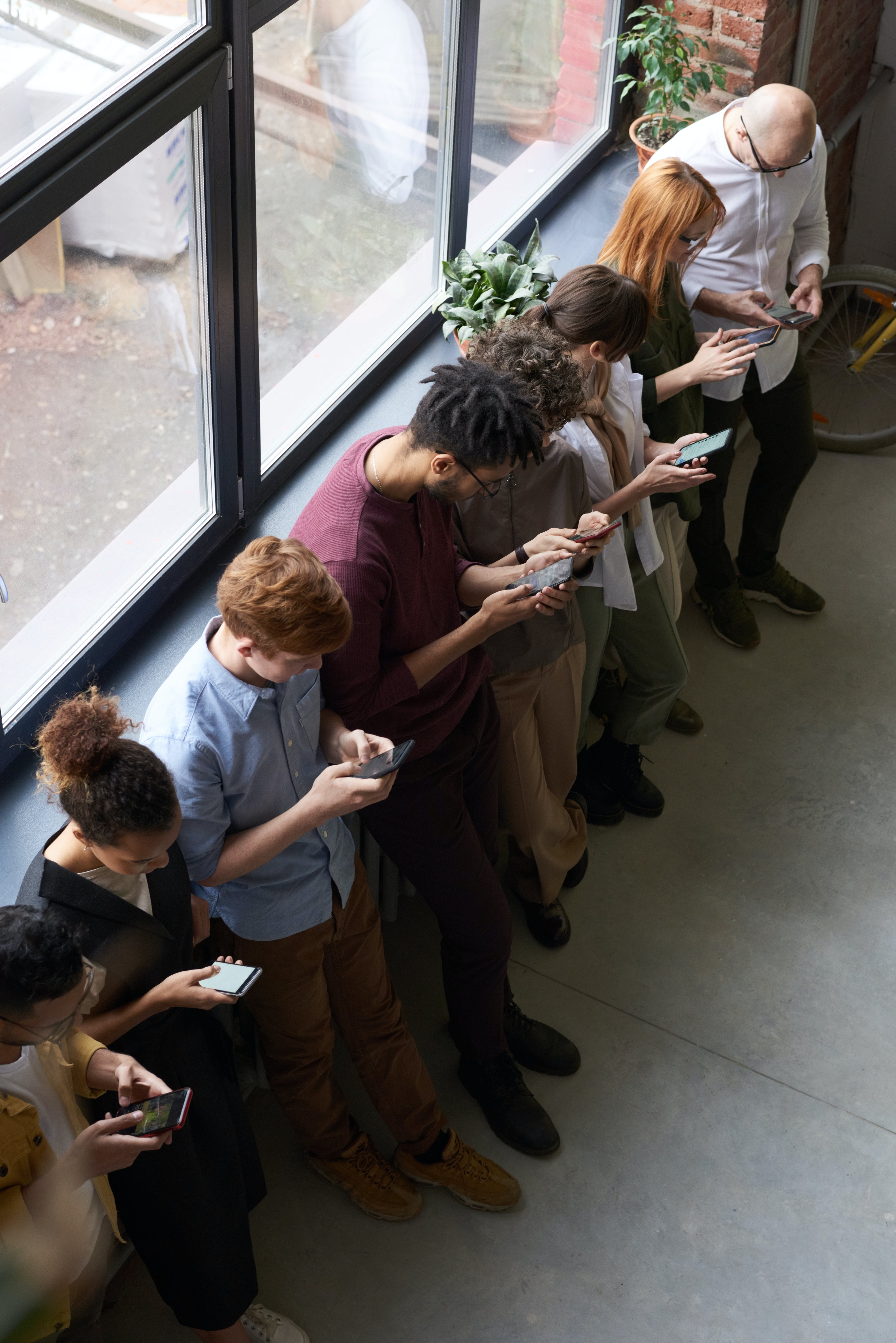 Personas haciendo cola mientras manejan sus teléfonos inteligentes. | Fuente: Pexels
