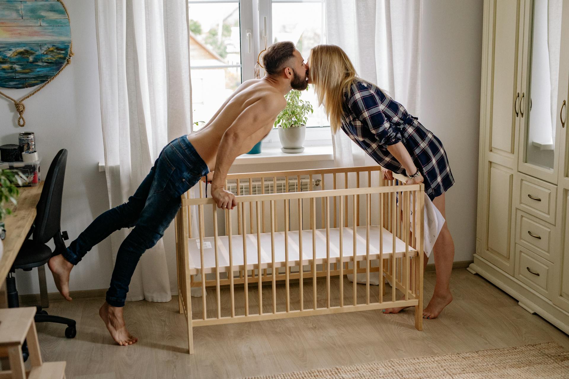 Una coppia si bacia mentre allestisce una culla per bambini | Fonte: Pexels