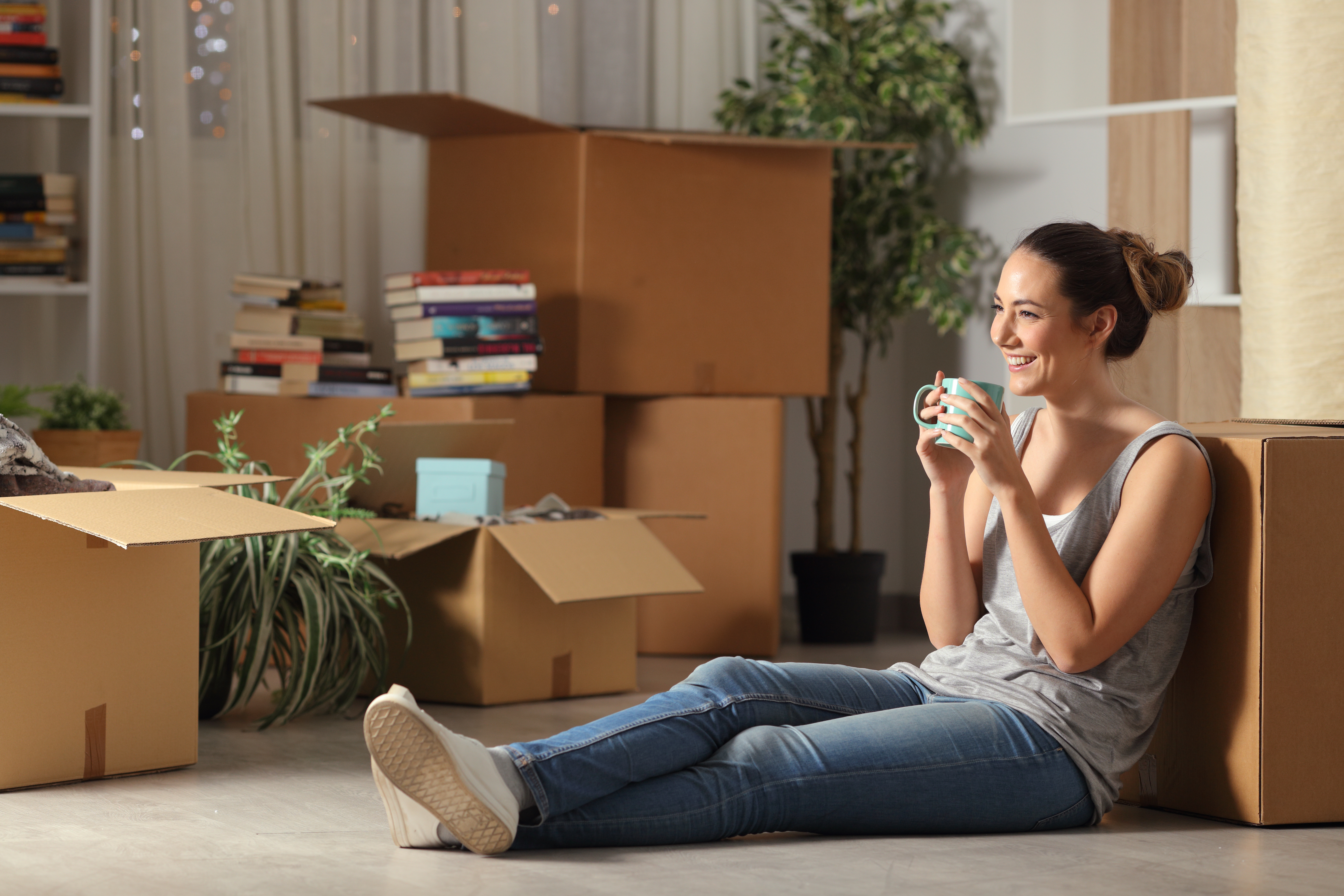 Una joven sentada en el suelo, rodeada de cajas de mudanza, bebiendo café. | Foto: Shutterstock