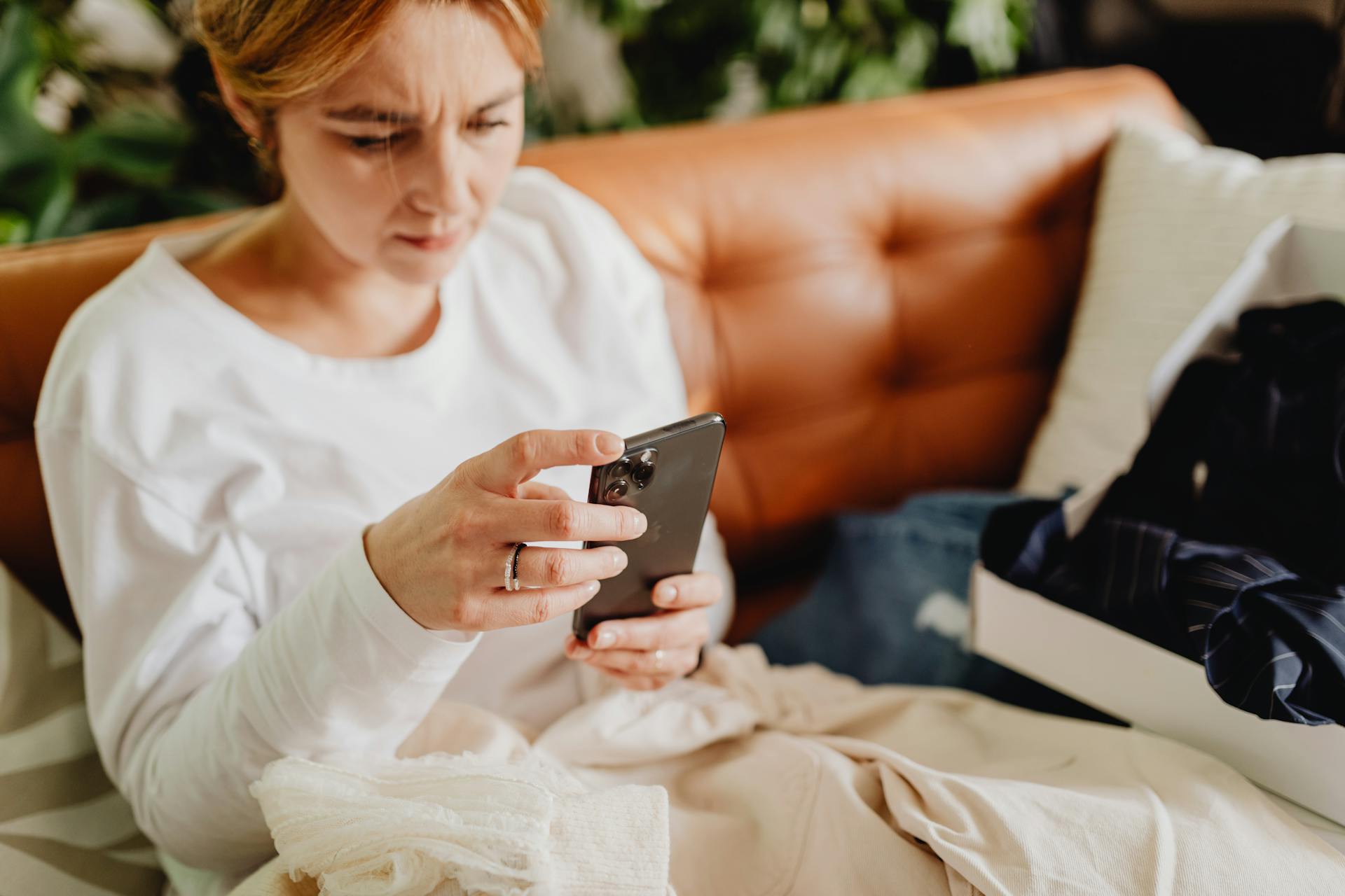 Una mujer sentada en el sofá y sujetando su smartphone | Fuente: Pexels