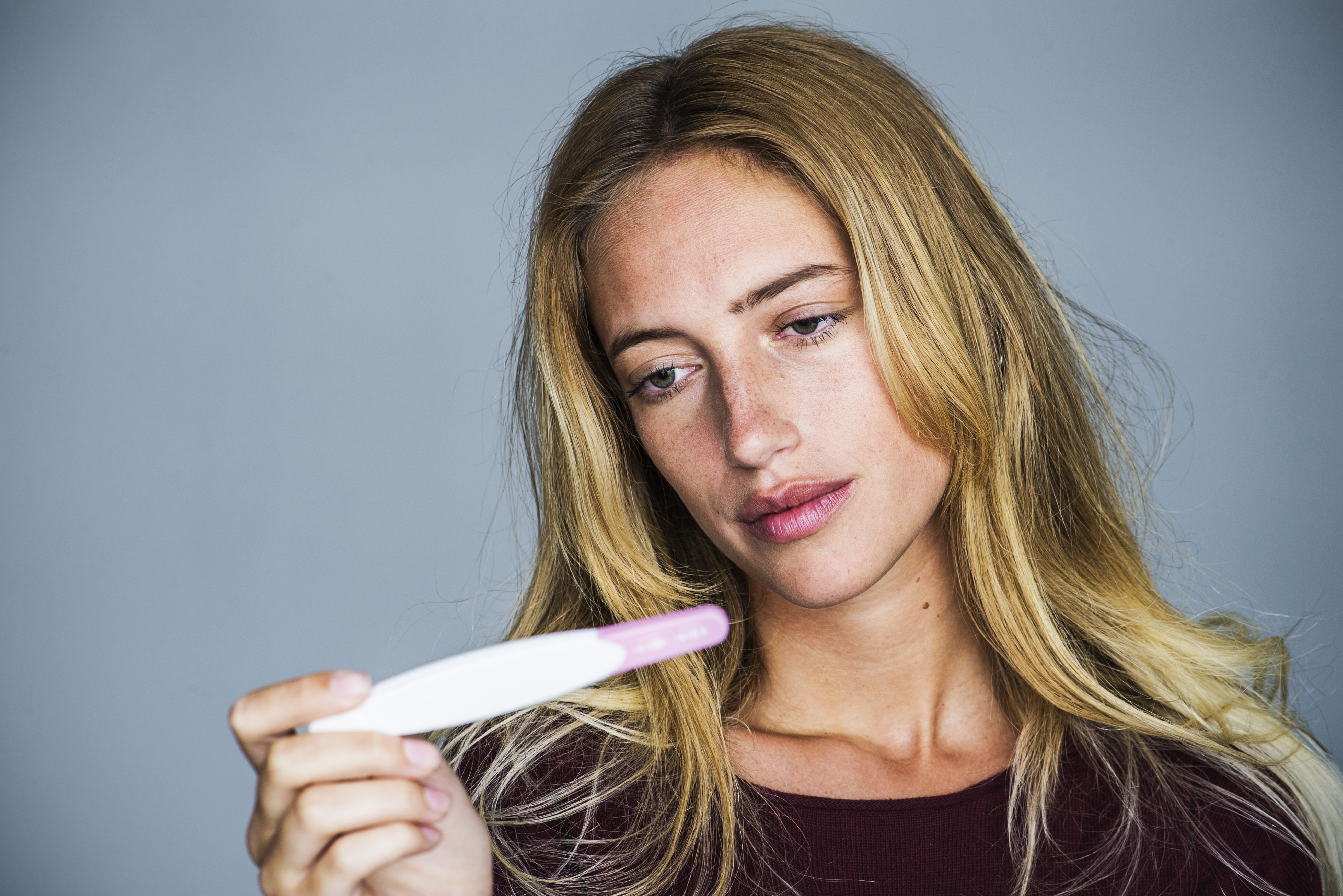 Mujer joven mirando un test de embarazo con expresión decepcionada | Foto: Getty Images