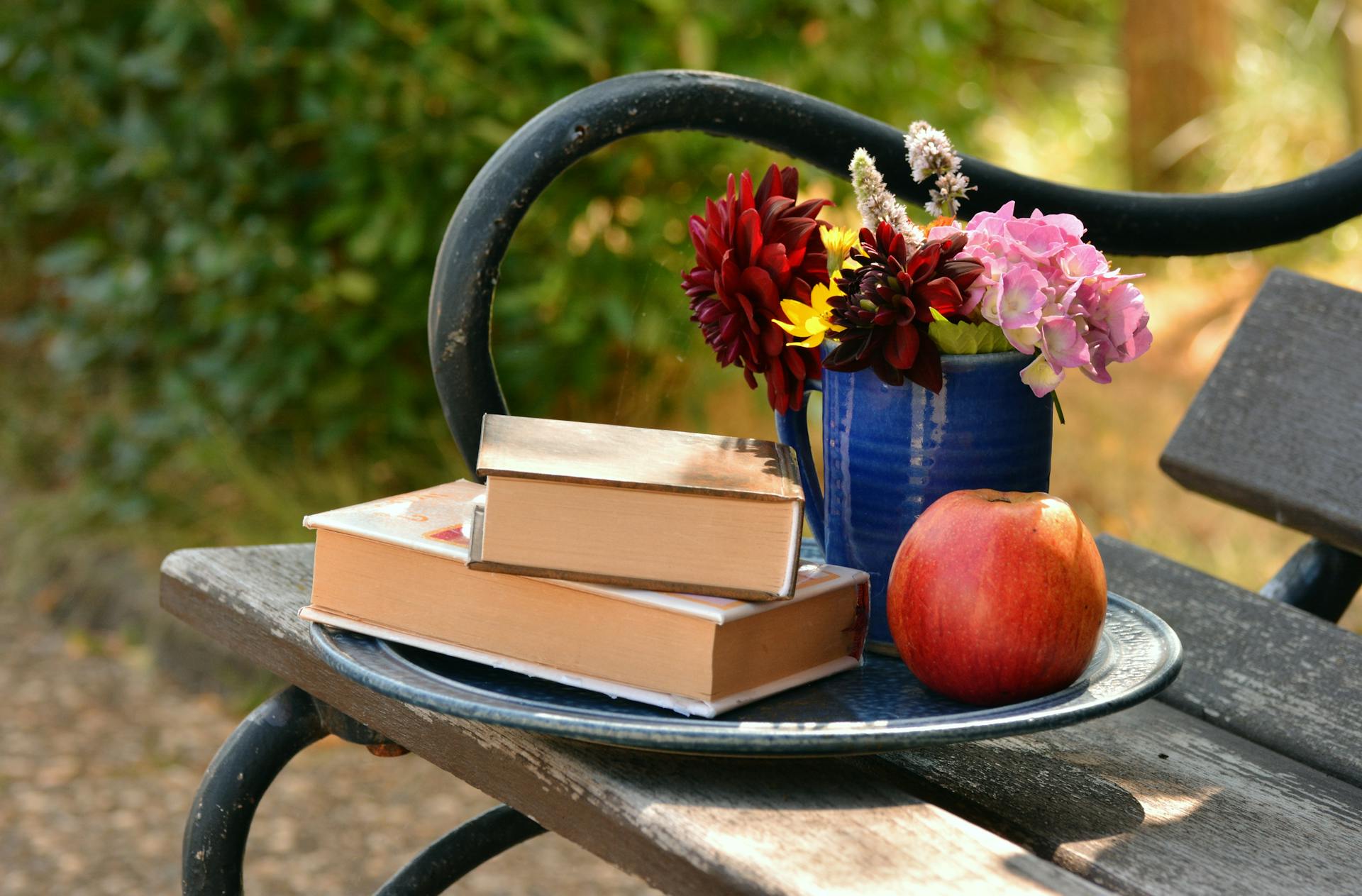 Dos libros colocados uno encima del otro junto a un jarrón de flores y una manzana roja | Foto: Pexels