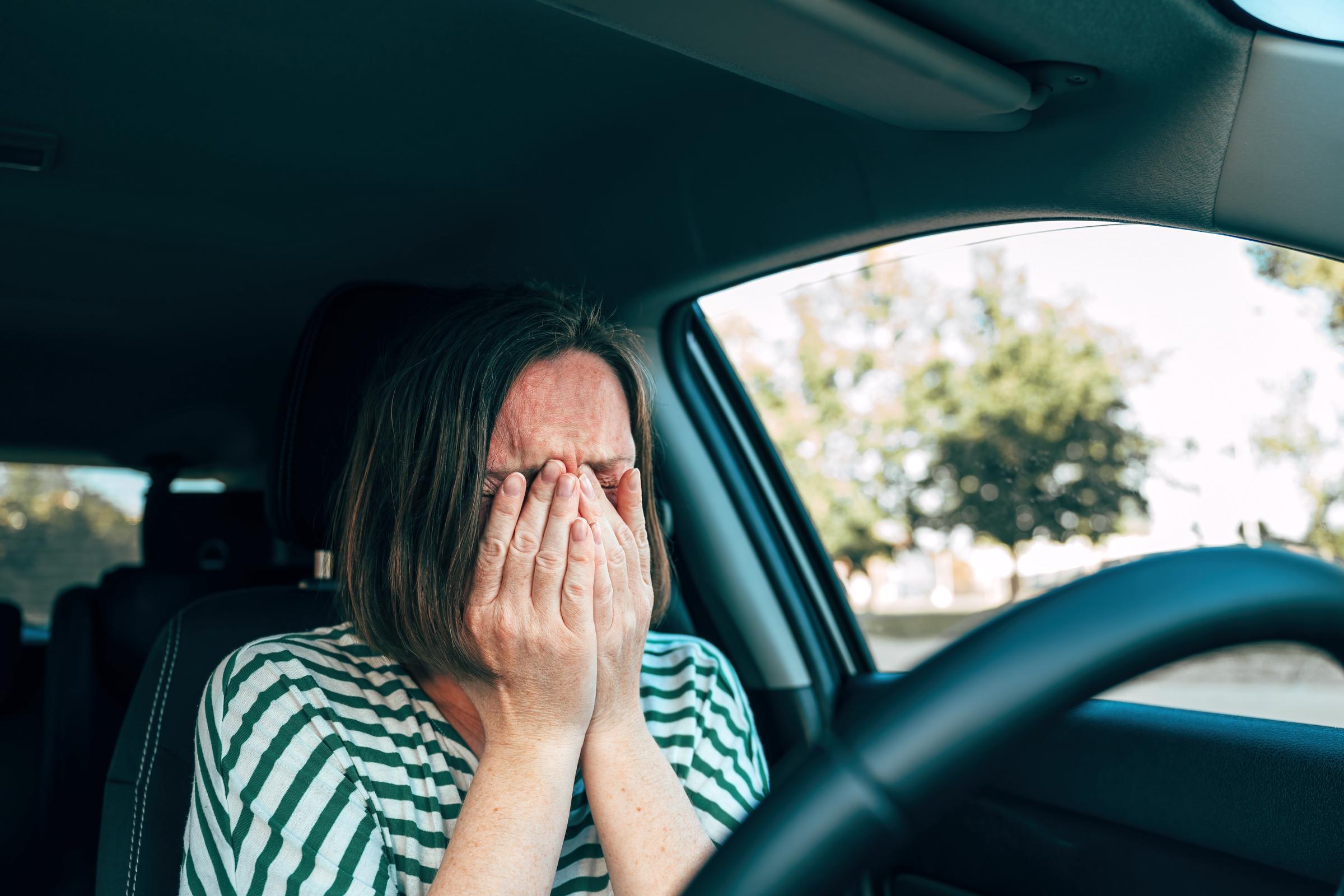 Mujer llorando con sus manos en su rostro mientras está sentada dentro de un vehículo estacionado | Fuente: Shutterstock