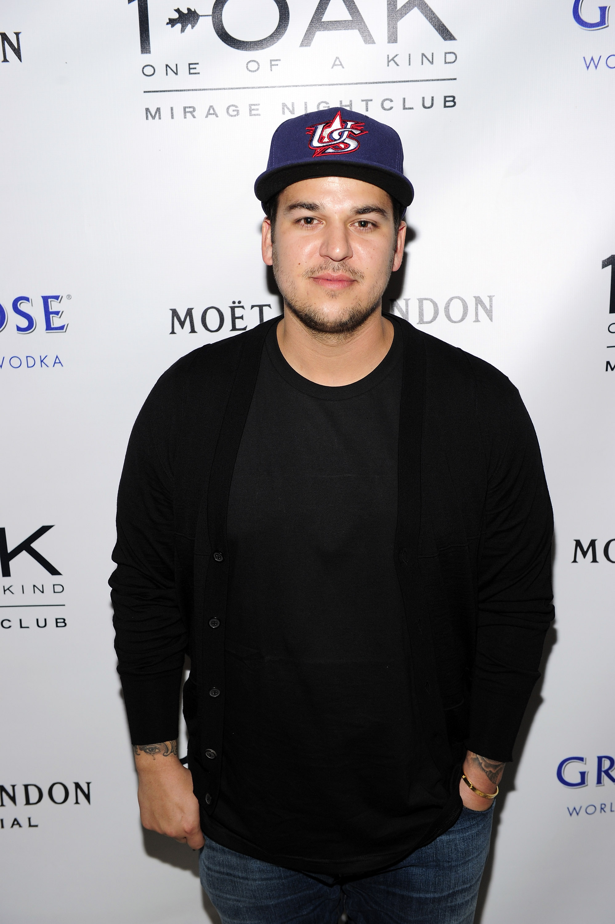 Rob Kardashian posa con una camiseta negra, un cárdigan y una gorra de béisbol en la discoteca 1 OAK de Las Vegas en mayo de 2013. Su aparición tuvo lugar en un momento en el que sus cambios de peso estaban siendo objeto de escrutinio público, lo que afectaba a su confianza y a sus ganas de asistir a eventos. | Fuente: Getty Images.
