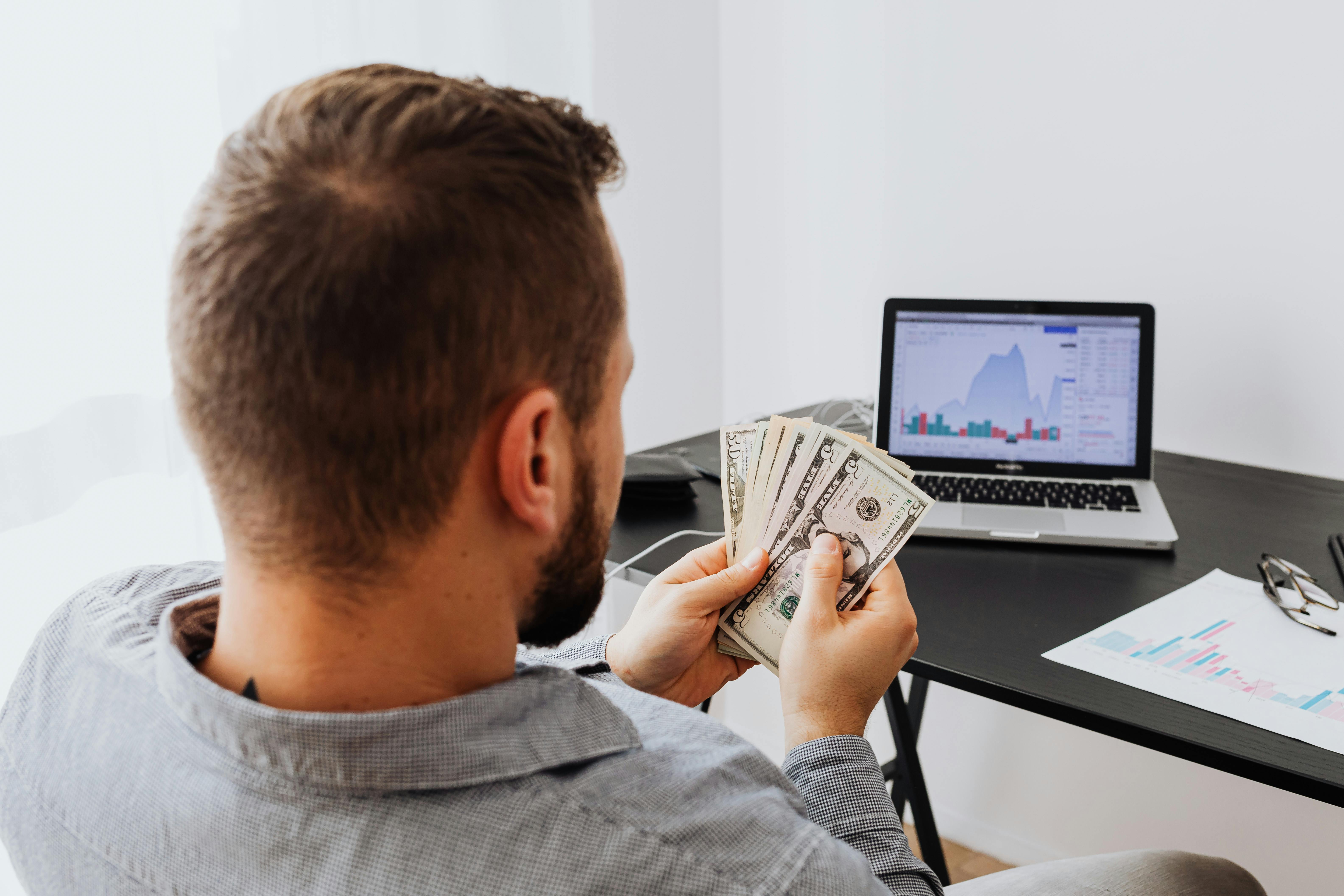 Hombre contando dinero frente a la portátil | Foto: Pexels