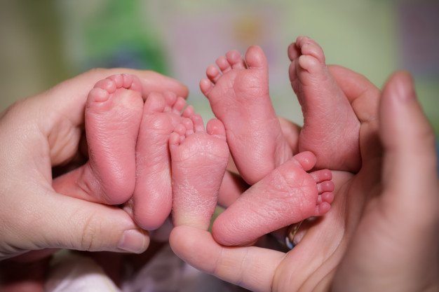 Persona sosteniendo los pies de tres bebés. │Foto: Freepik