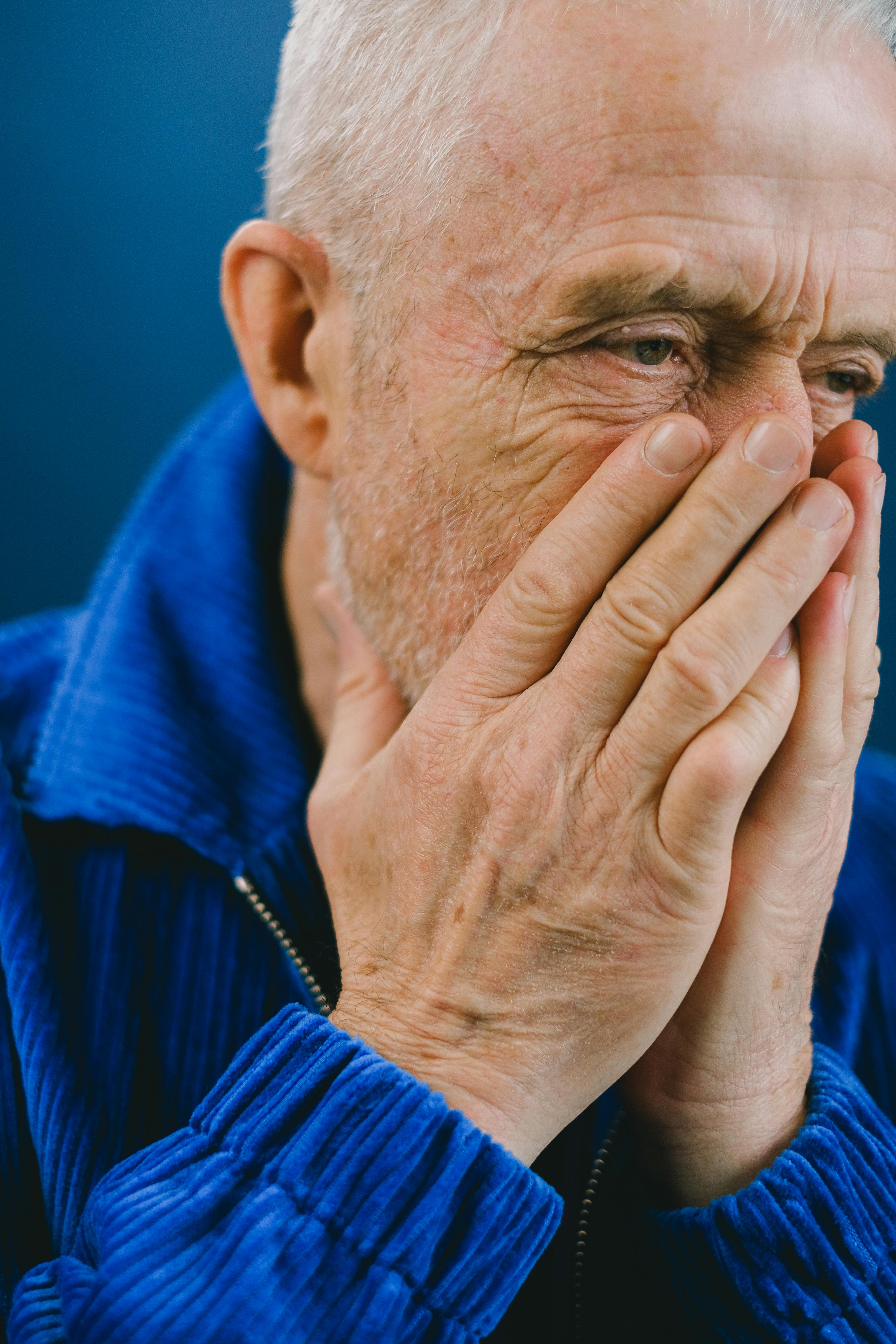 Un anciano alterado tapándose la boca y la nariz con las manos | Fuente: Pexels