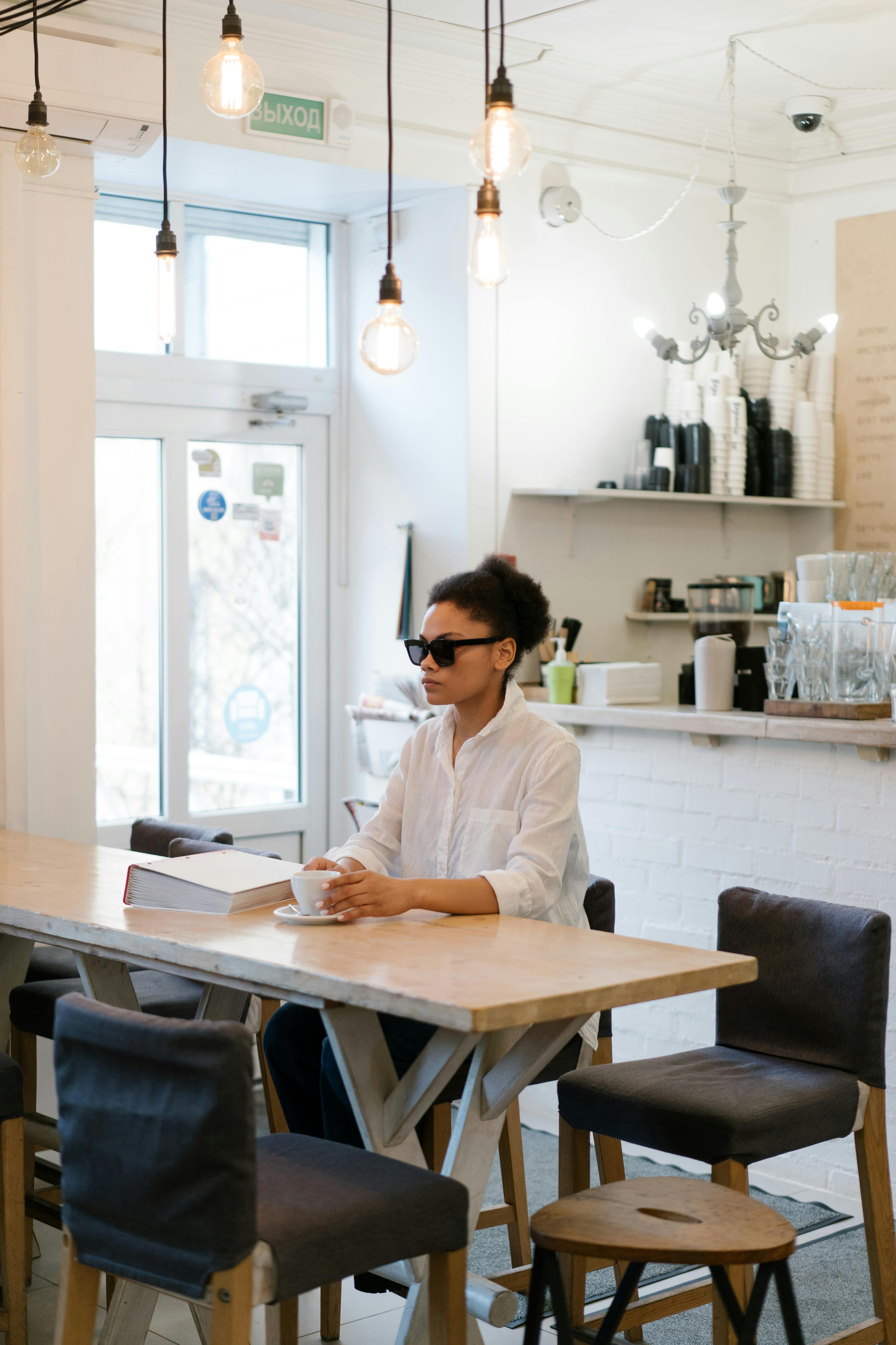 Mujer con gafas de sol sentada en la mesa de un café | Foto: Pexels