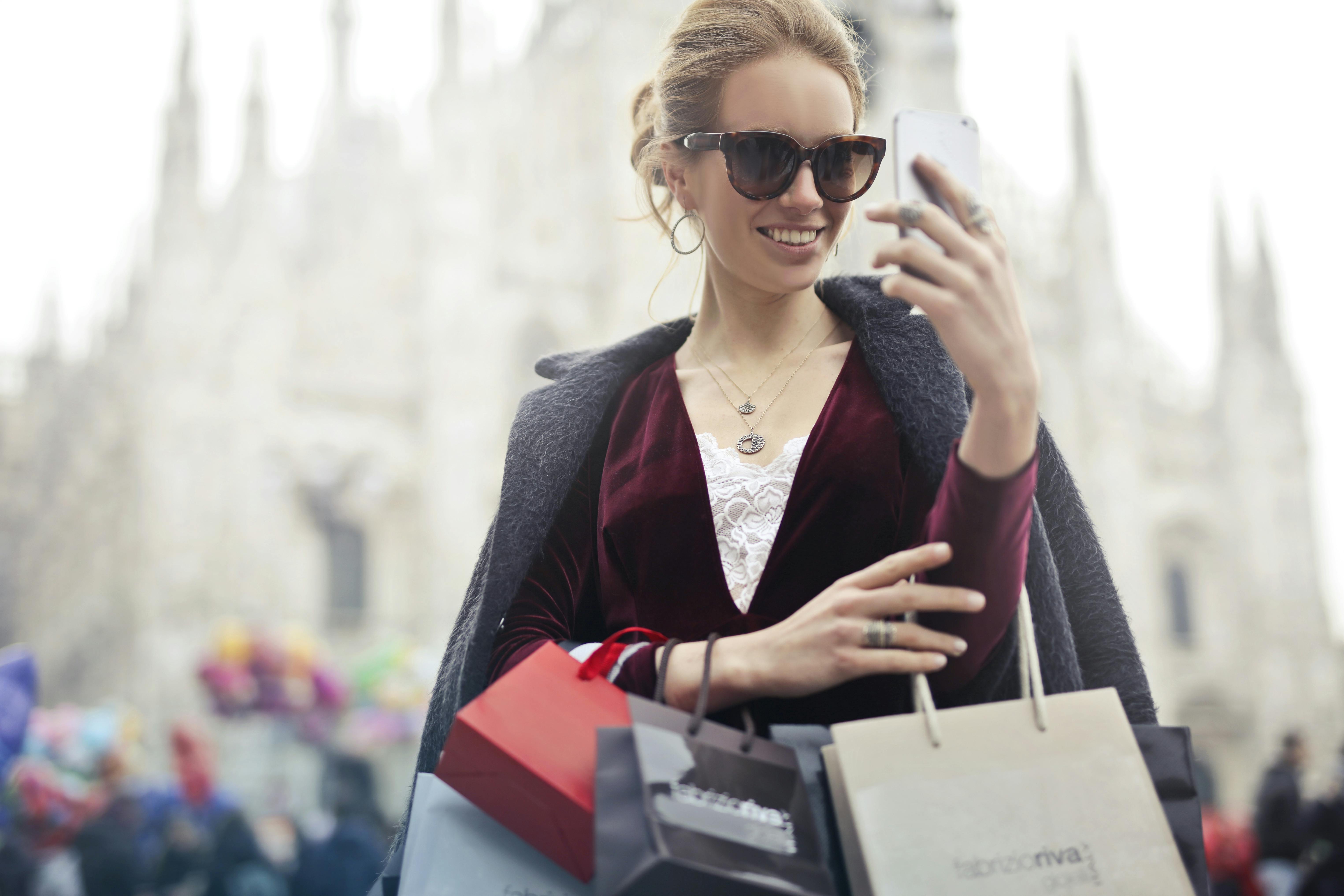 Mujer con bolsas de compra mira el móvil | Foto: Pexels