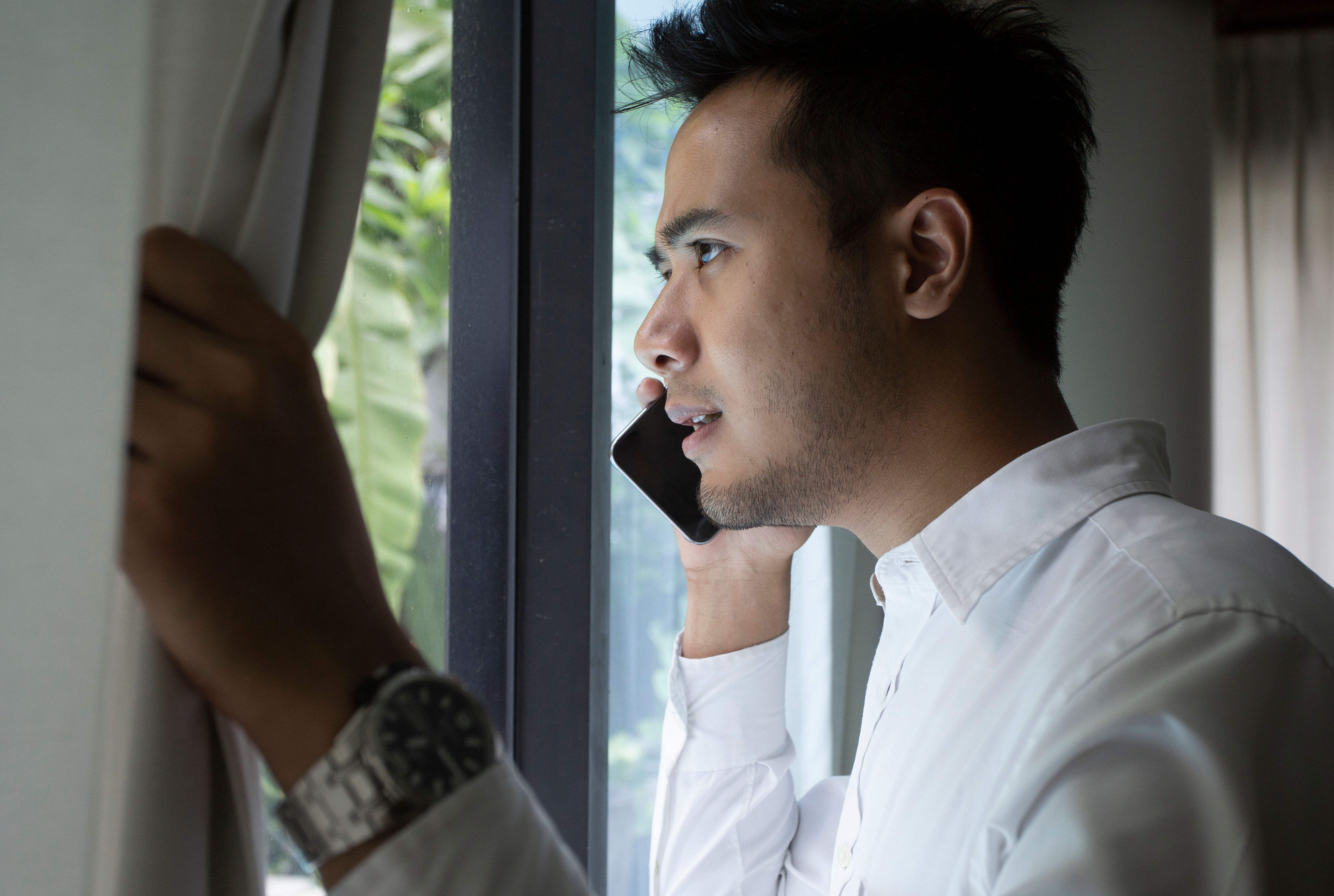 Un hombre habla por teléfono cerca de la ventana | Fuente: Shutterstock.com