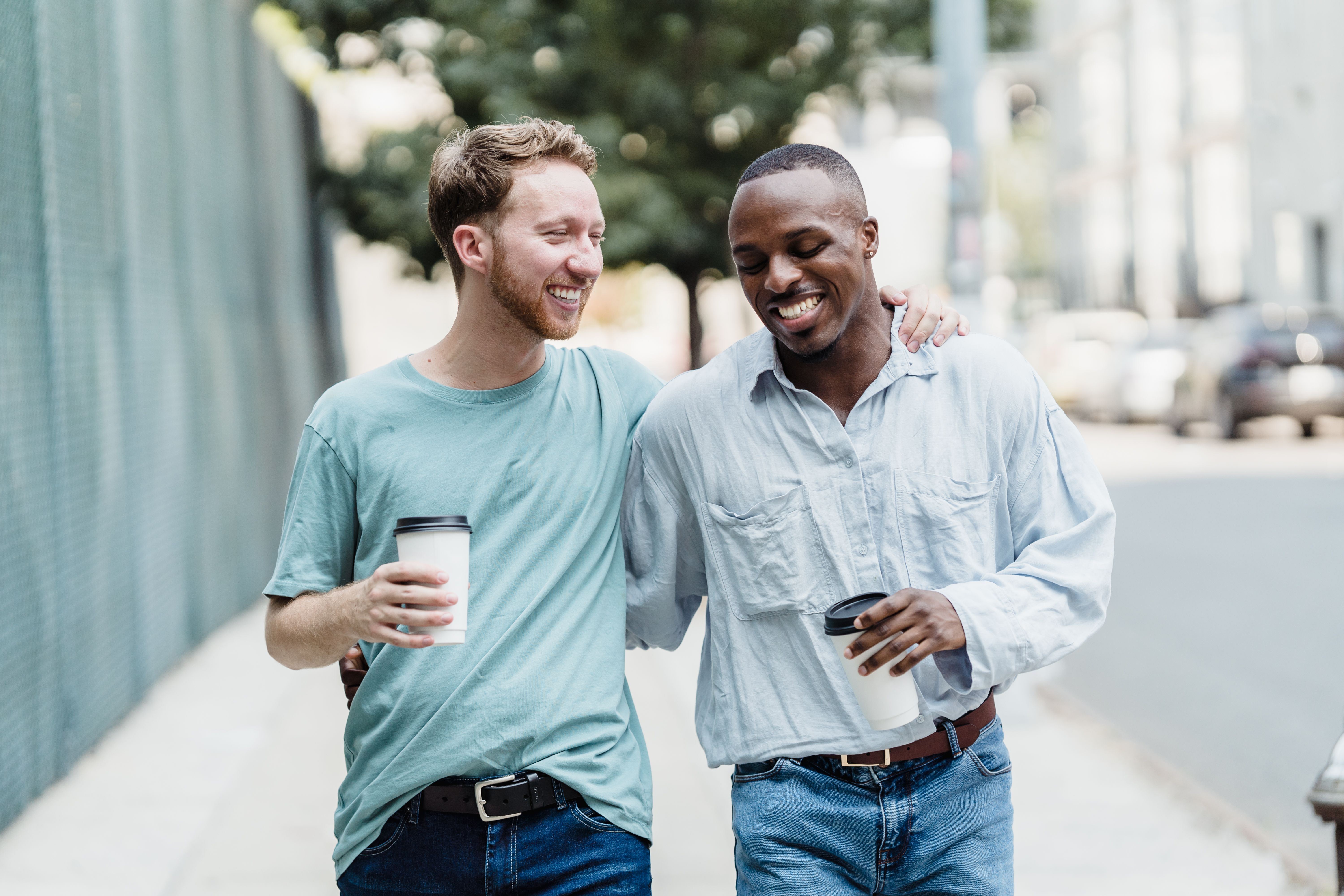Dos amigos paseando y riéndose por una calle de la ciudad, disfrutando juntos de un café al aire libre | Fuente: Pexels