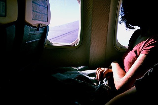Mujer sentada en el avión mirando hacia la ventana. | Foto: Pixabay.